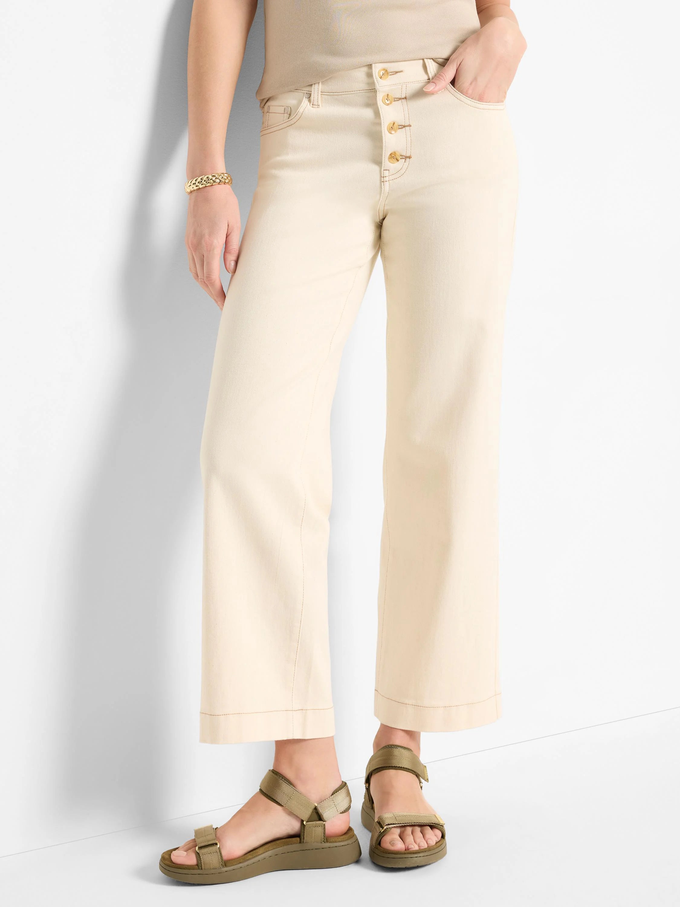Off-white wide-leg jeans with gold buttons. Jeans have a slight cuff. Model wears olive green sandals.