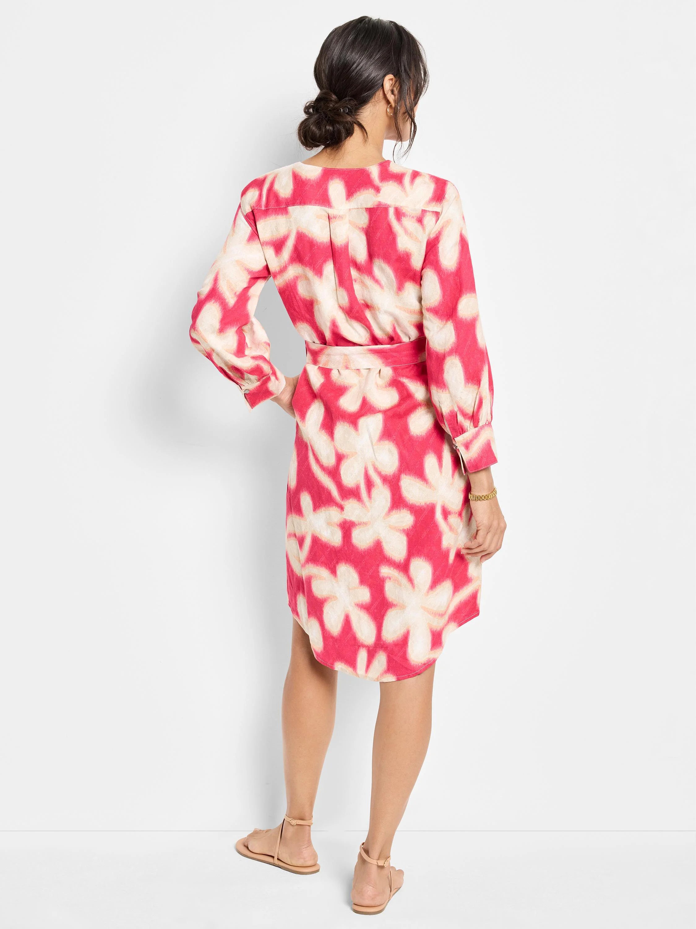 Pink shirt dress with a belted waist. Features a light beige flower print. Long sleeves. Knee-length.