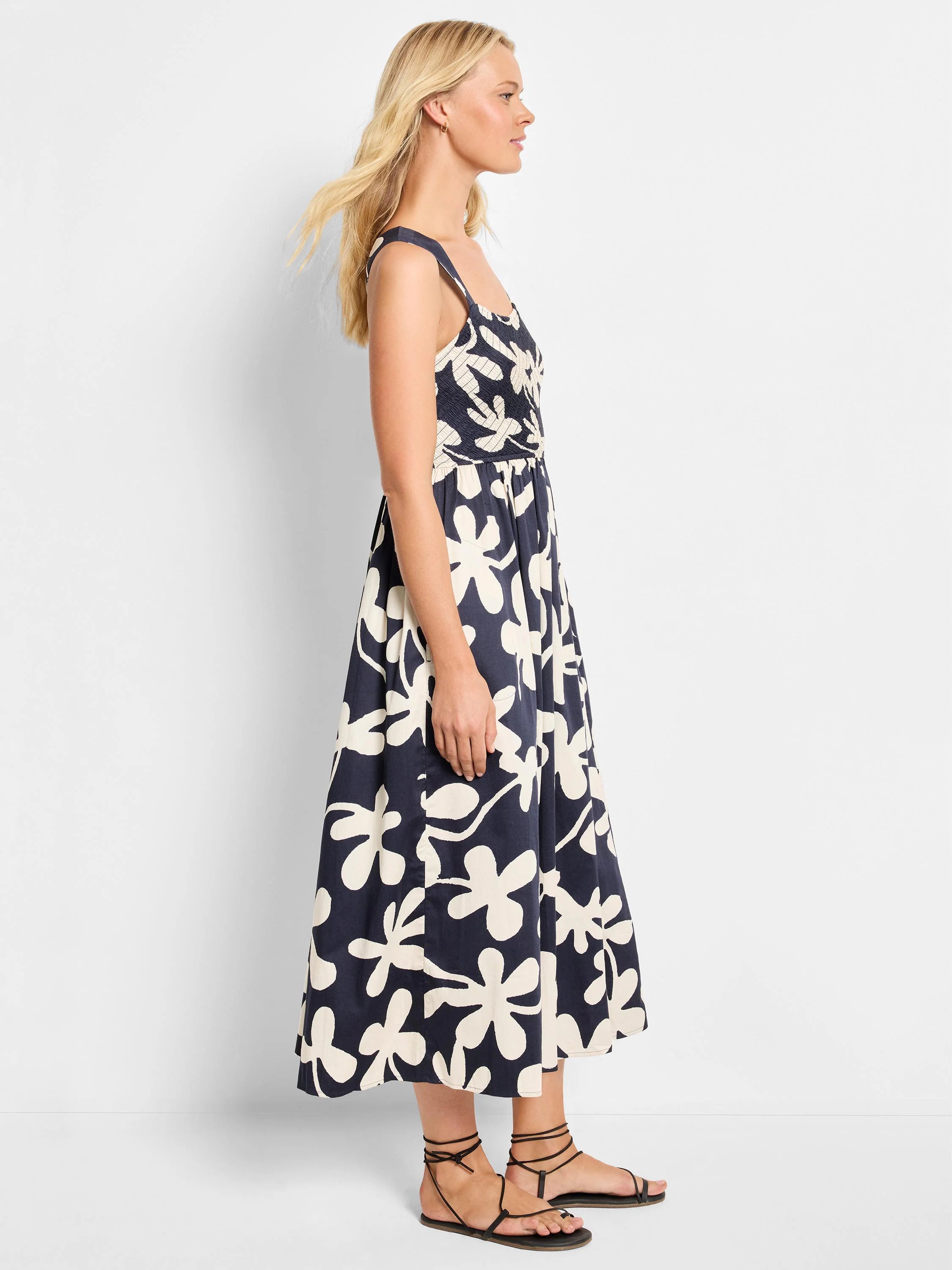 Midi-length sleeveless dress. Dark navy background with large off-white stylized floral print. Square neckline, smocked...
