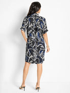 Black short-sleeve shirt dress with white and dark blue abstract leaf print.  Shown from the back.