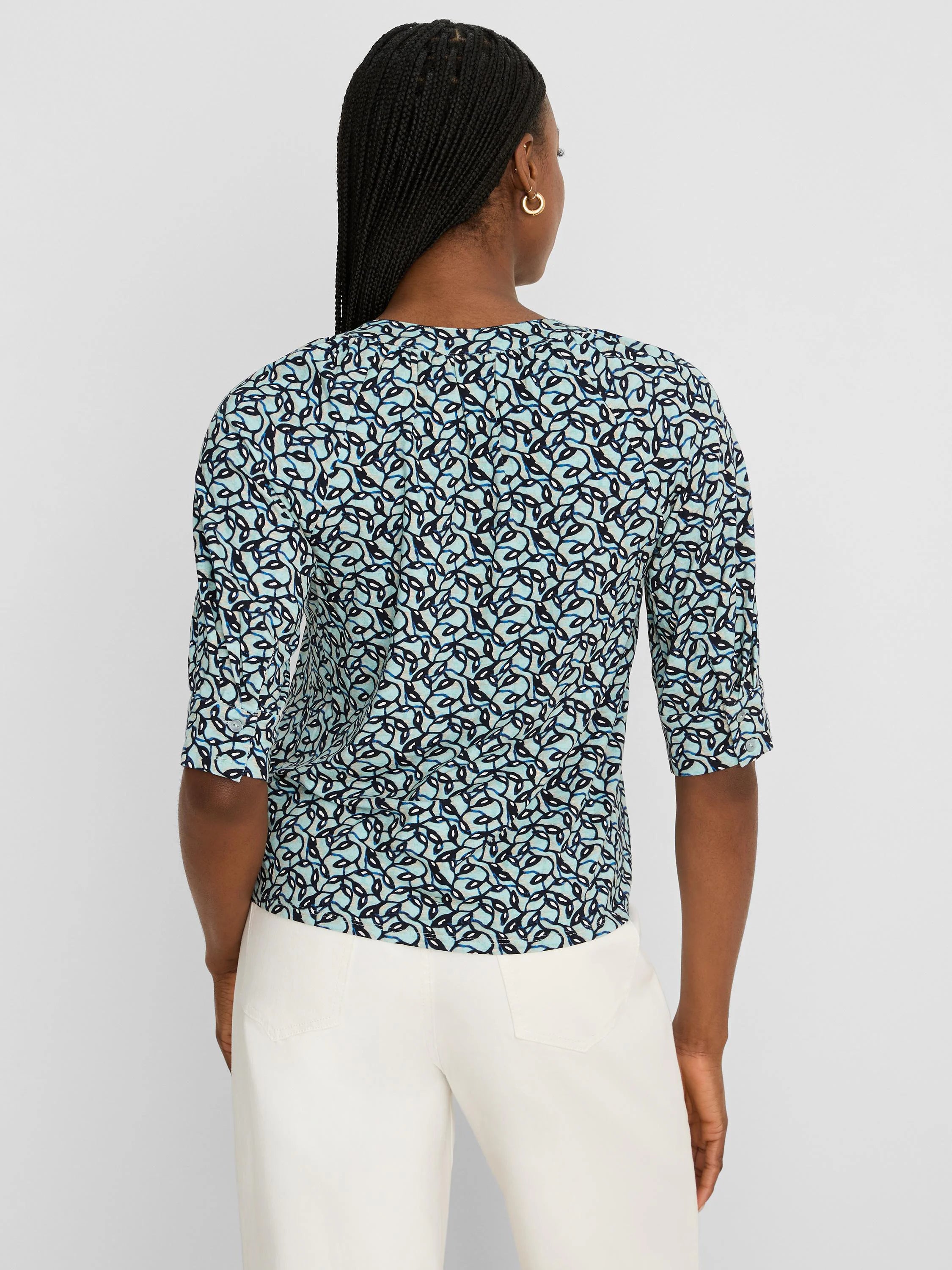 Light blue top with dark blue & white abstract vine pattern. Elbow-length sleeves, rolled tabs. View from back.