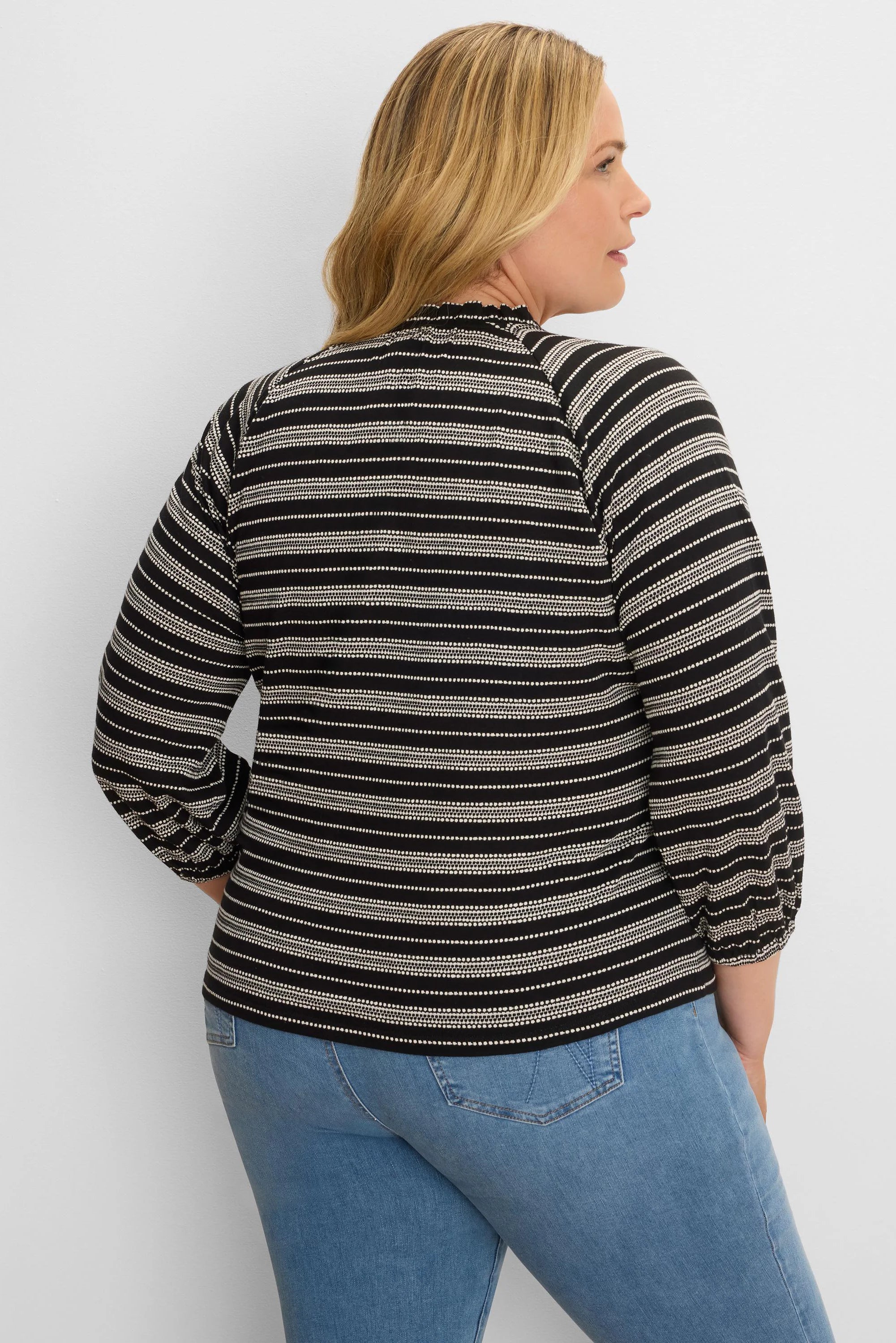 Black & off-white knit top with varied horizontal stripes, ruffled mock neck, and long sleeves with gathered cuffs.