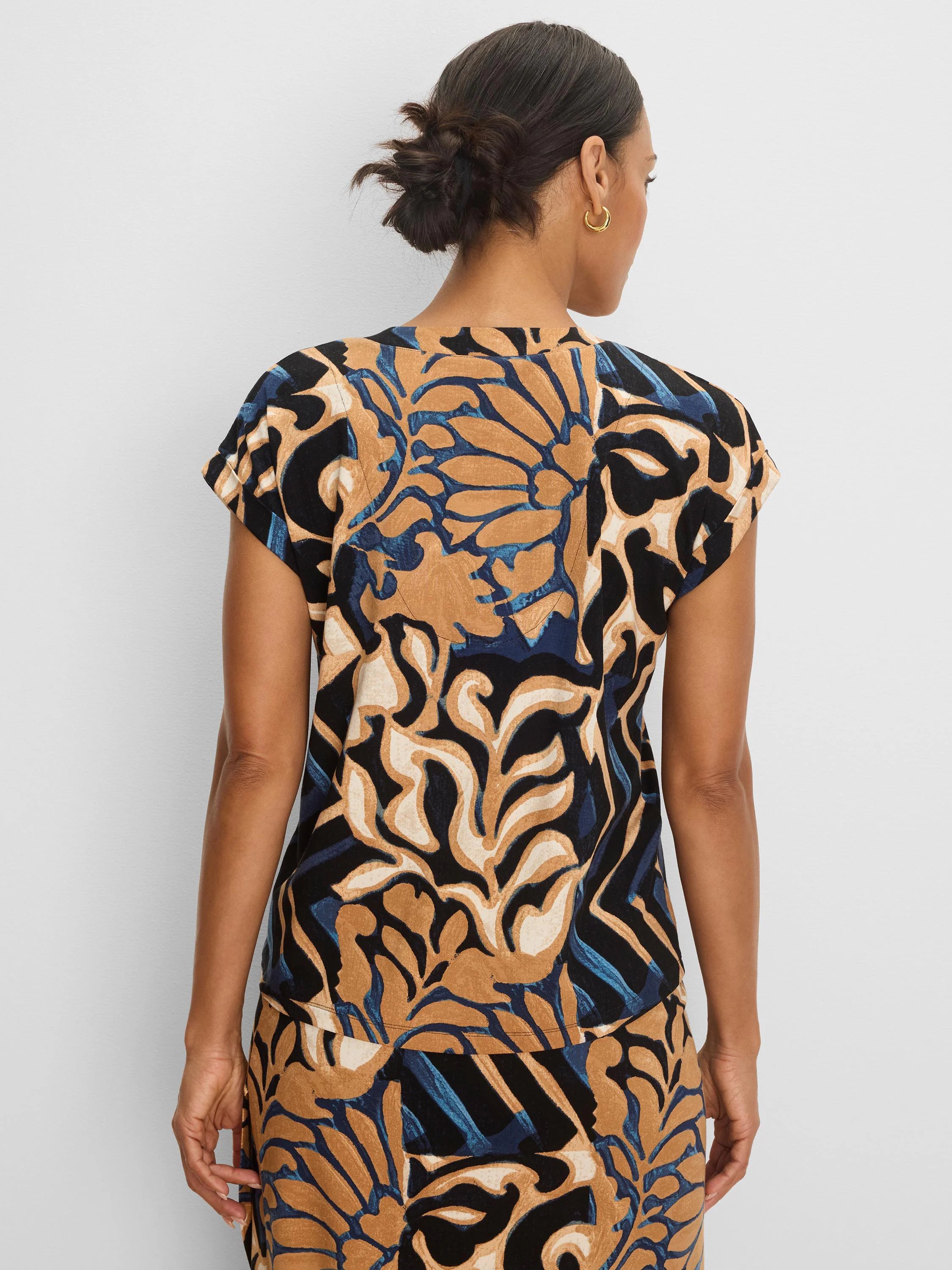 Cap sleeve tee with abstract tan, black, blue, and cream deco blooms pattern, viewed from the back.