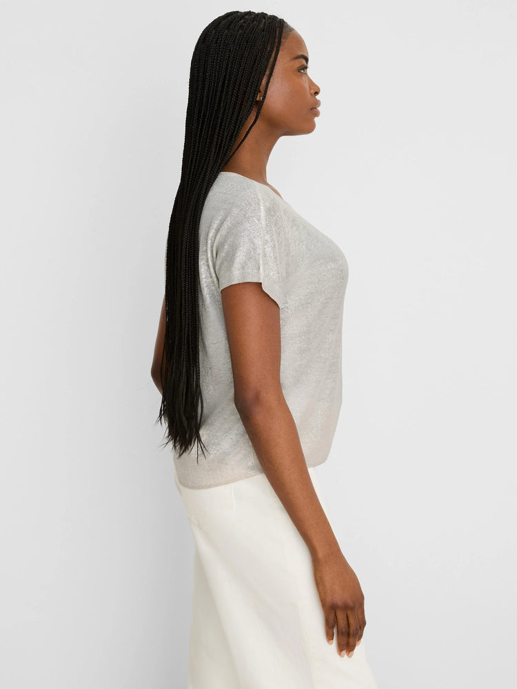 Shimmery champagne knit sweater with short sleeves. Loose fit, worn by a model in profile.