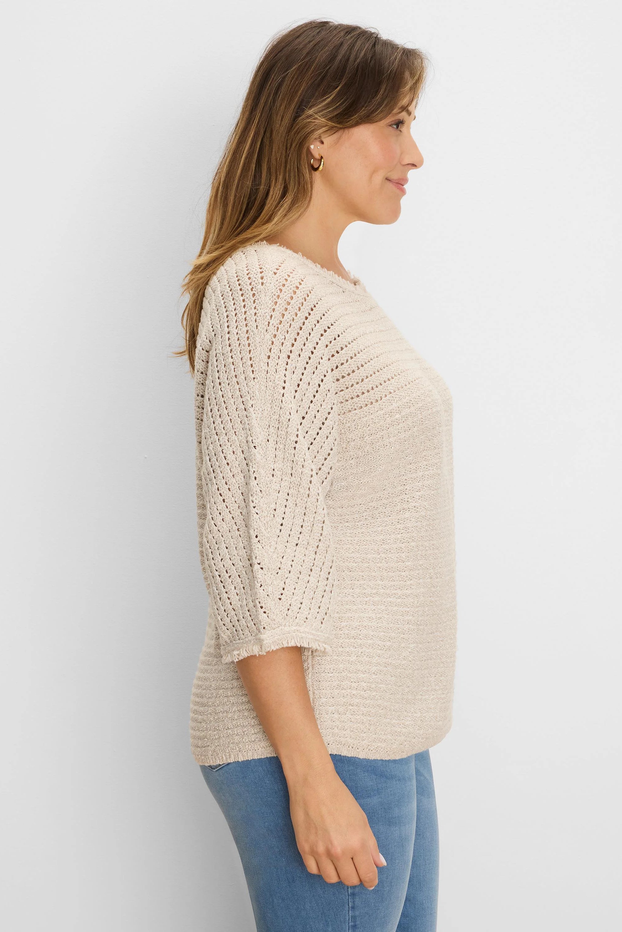 Cream-colored sweater with textured knit body and open-knit chevron 3/4 sleeves, featuring frayed cuffs.