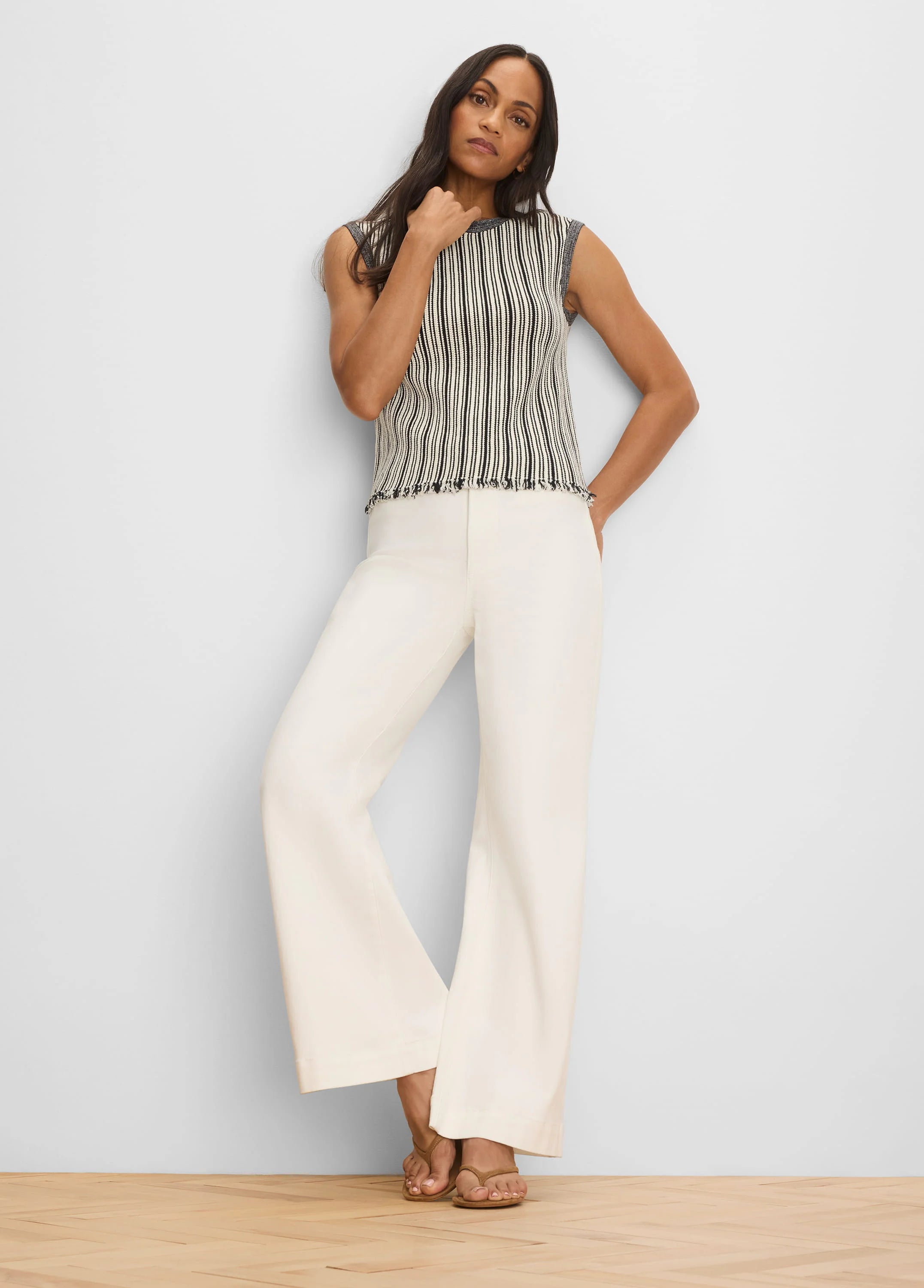 Sleeveless cream and black vertical striped sweater with a dark trim crew neck and fringed hem.