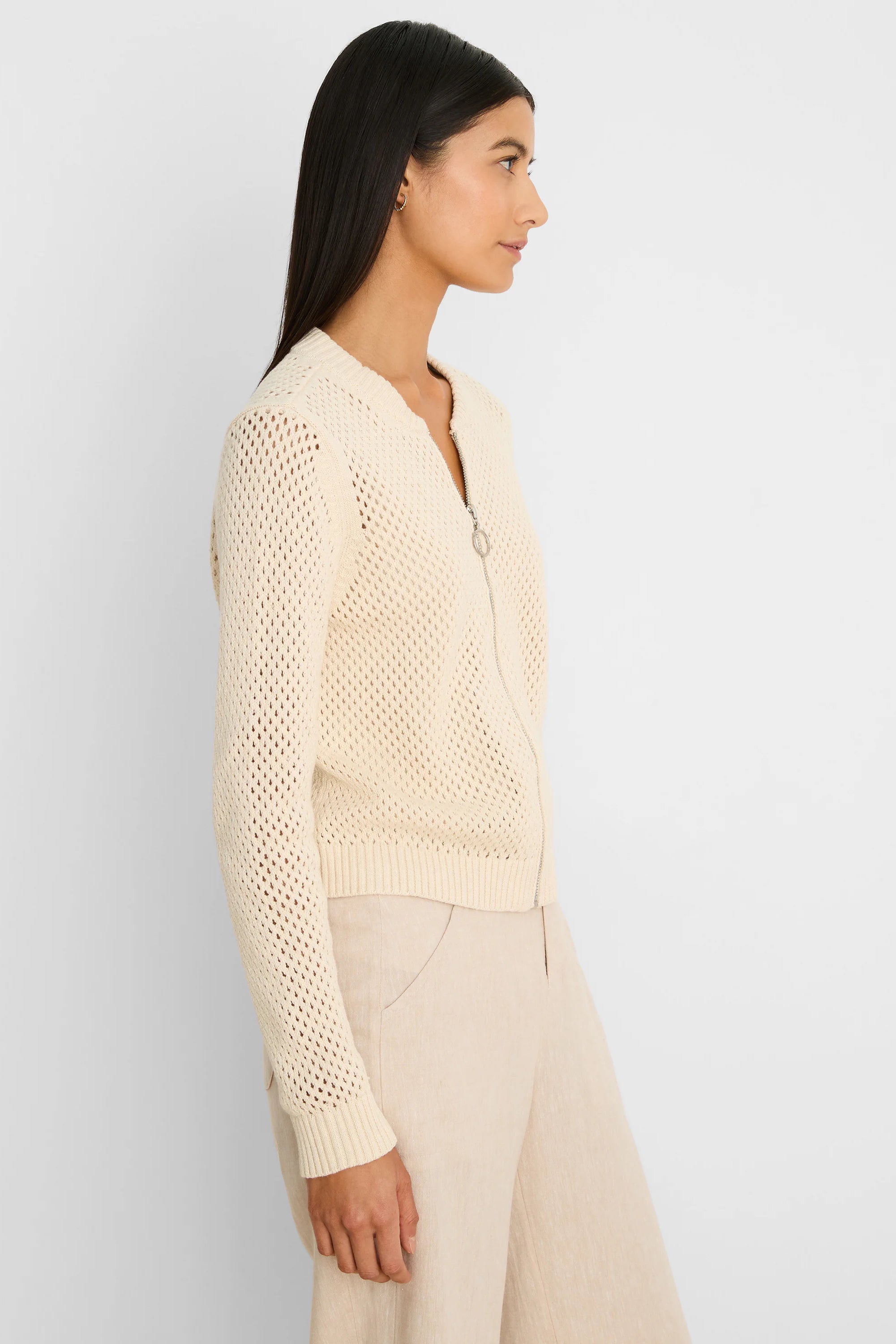 Cream open-knit zip-front cardigan with silver zipper pull, ribbed cuffs and hem, worn by a model.