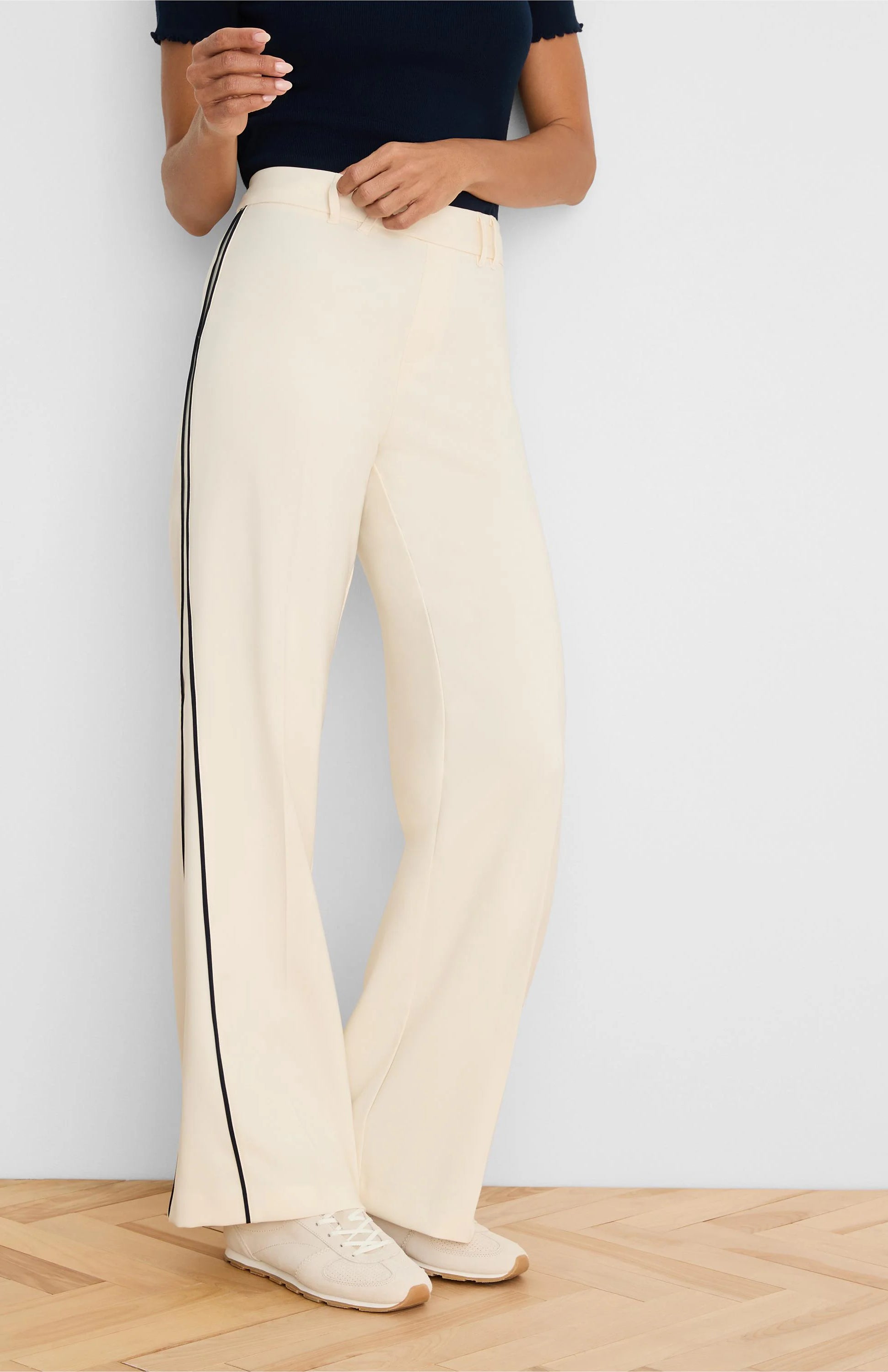 Cream wide-leg pants with a smooth, flowing drape and thin dark piping along each outer leg seam.
