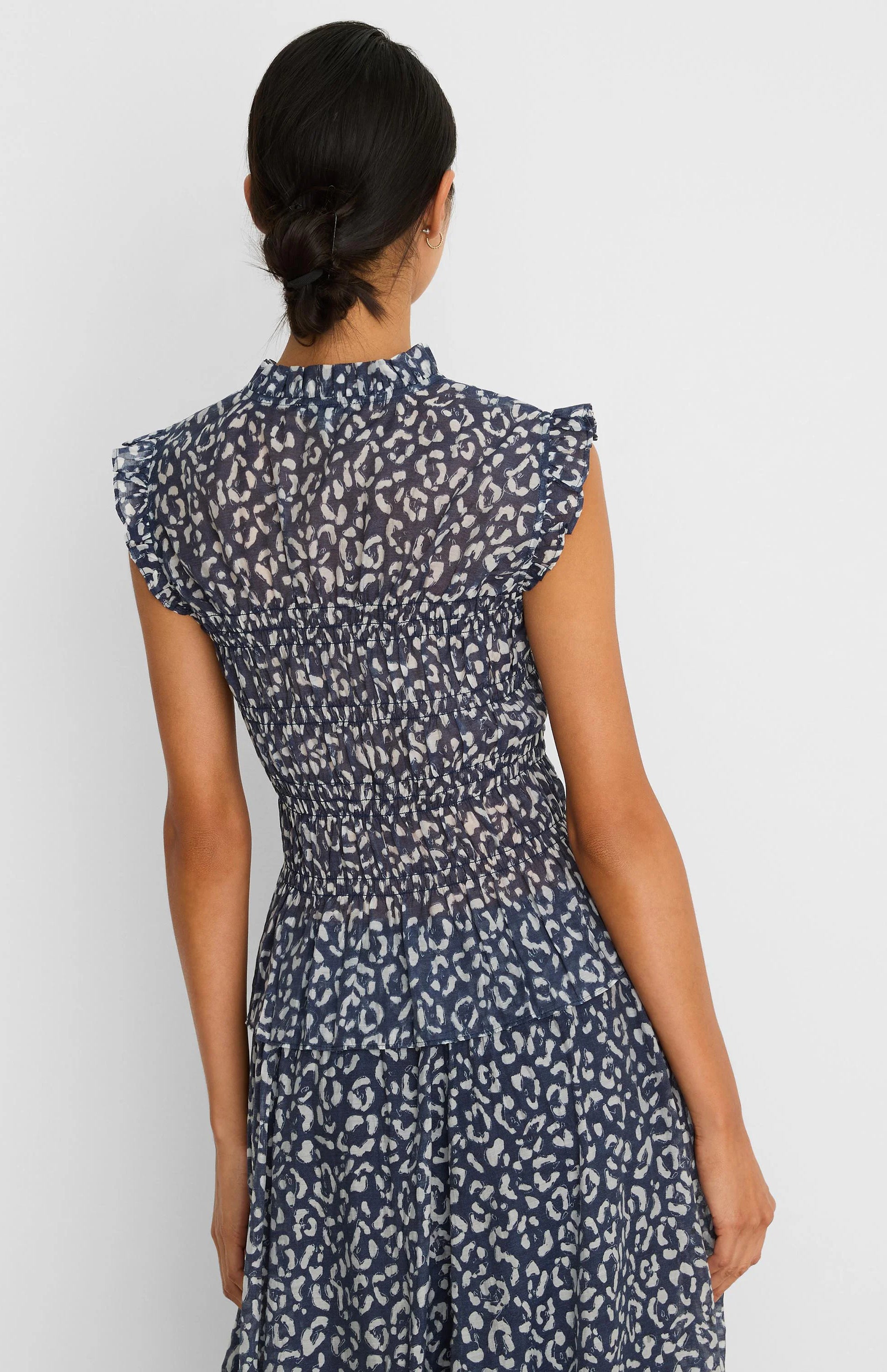 Indigo top with white abstract leopard print, smocked waist, ruffled mock neck, and cap sleeves.