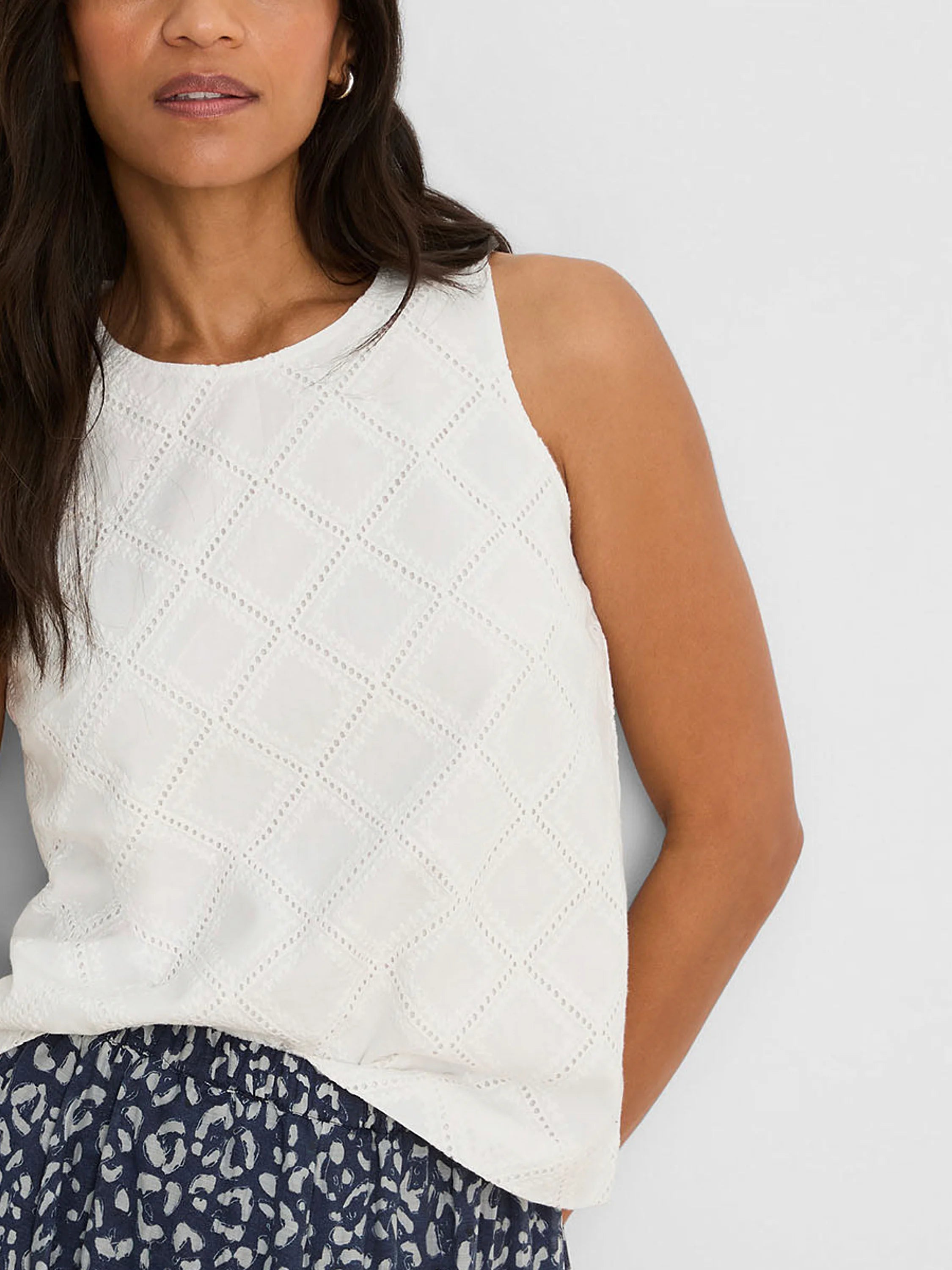 White sleeveless top with a rounded neckline and diamond eyelet pattern.