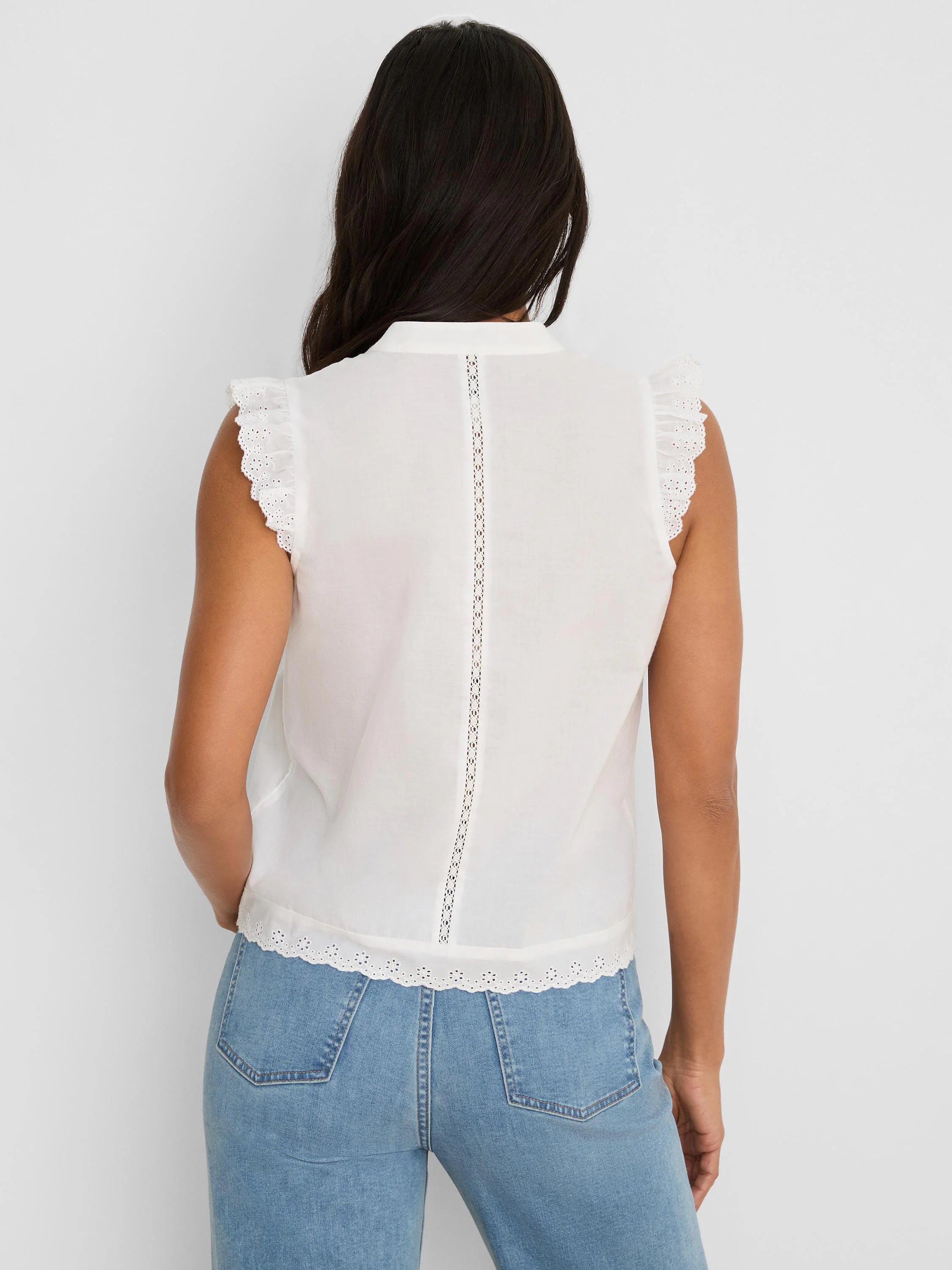 White sleeveless top with frilled eyelet lace shoulders, eyelet lace trim at hem, and vertical lace back detail.