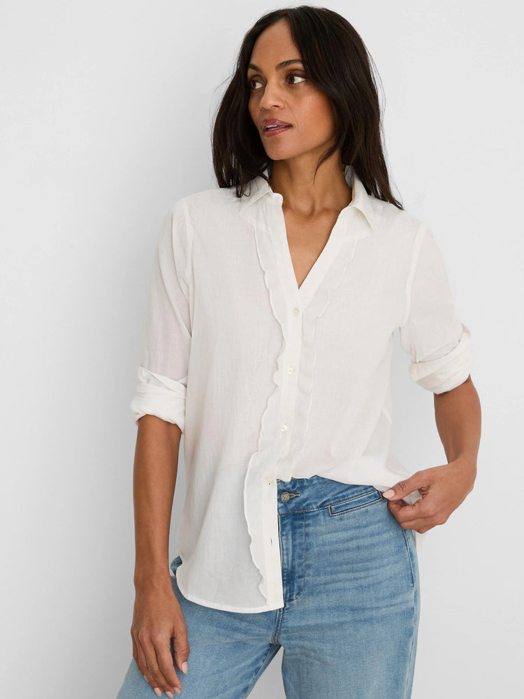 Off-white cotton shirt with wavy ruffles along the button placket, rolled sleeves, paired with light blue jeans.
