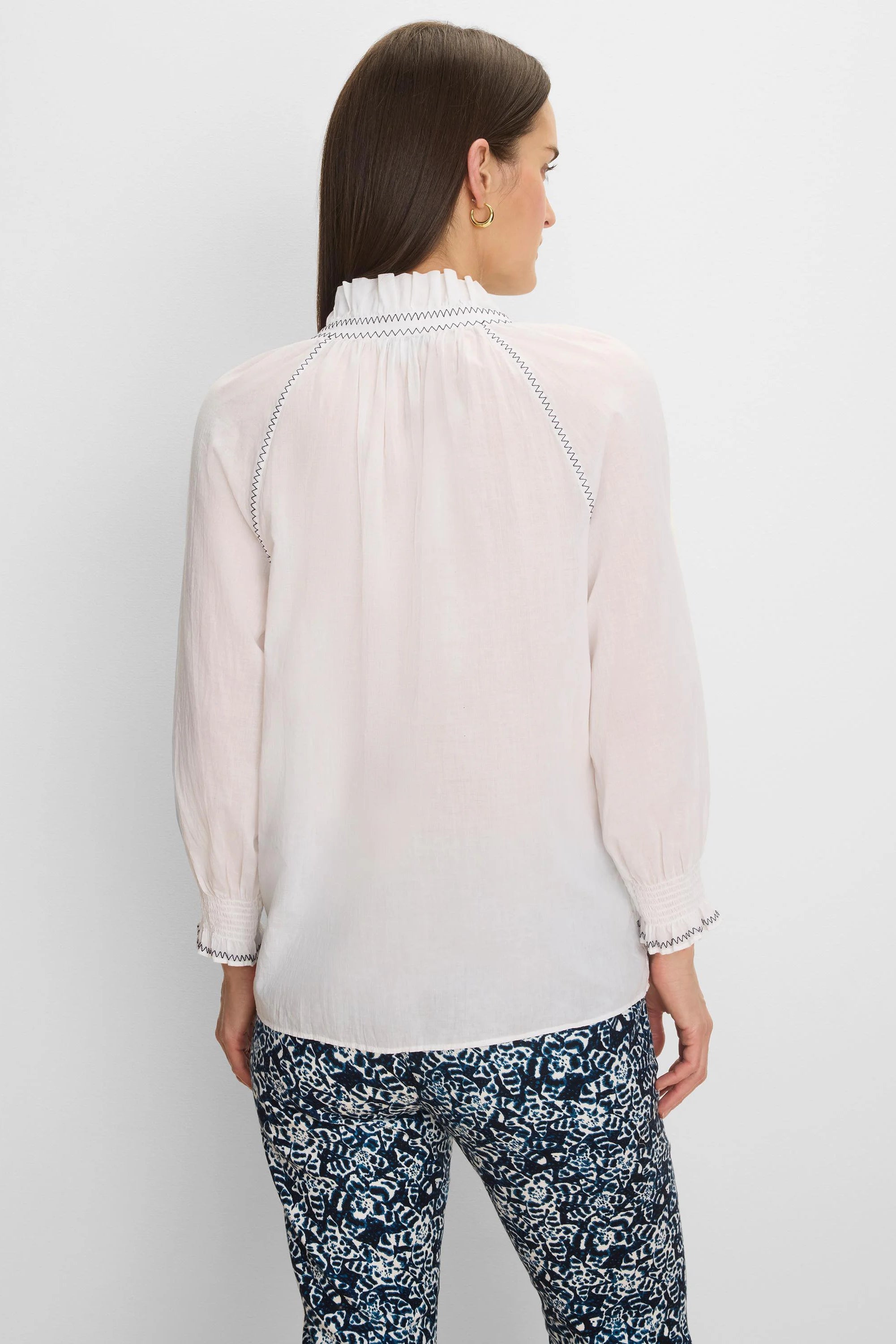 White crinkle shirt with dark zig-zag stitching on a ruffled high collar, back raglan seams, and smocked cuffs.