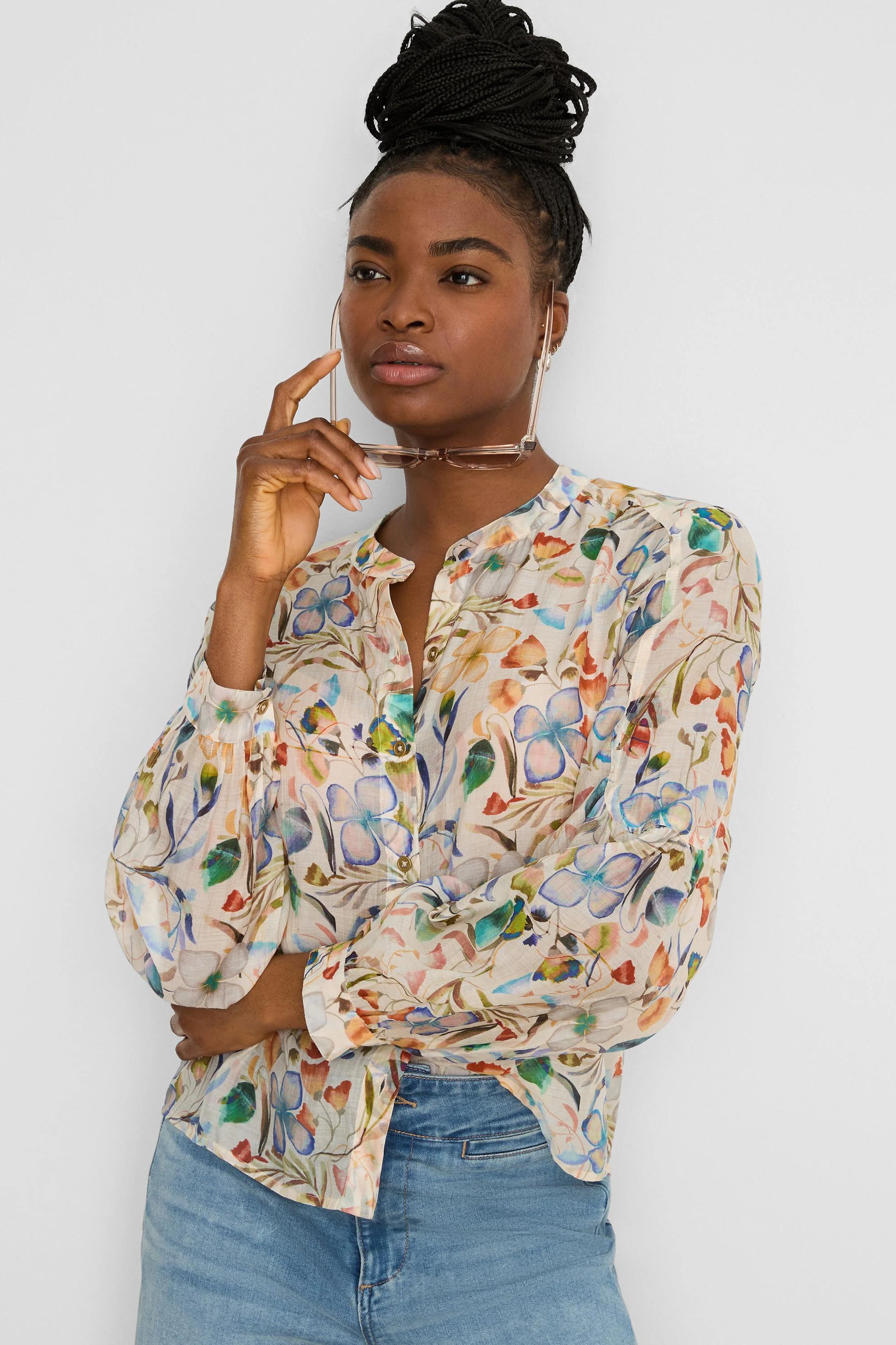 Cream shirt with a multicolored pressed floral print in blues, oranges, and greens. Features a band collar and blouson...