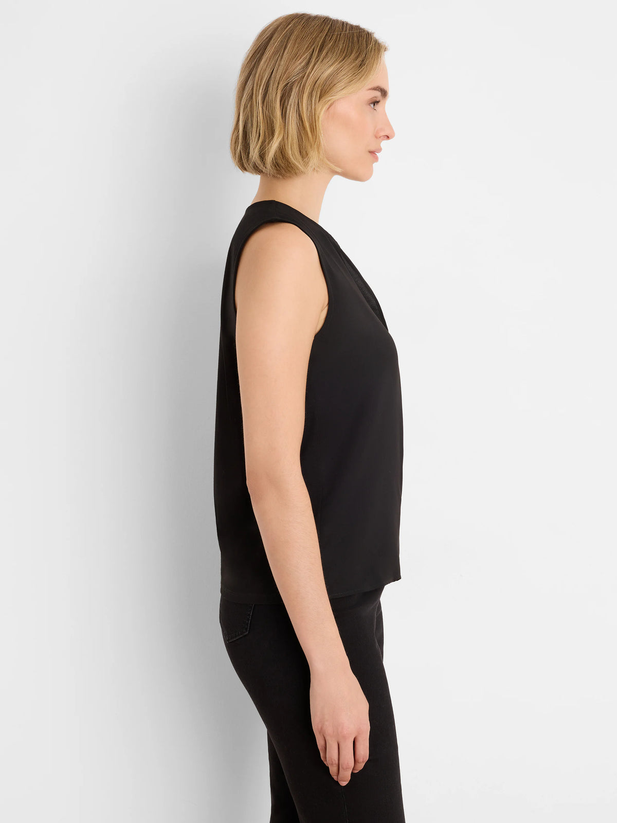 Black sleeveless top with a draped neckline, worn by a woman in side profile.