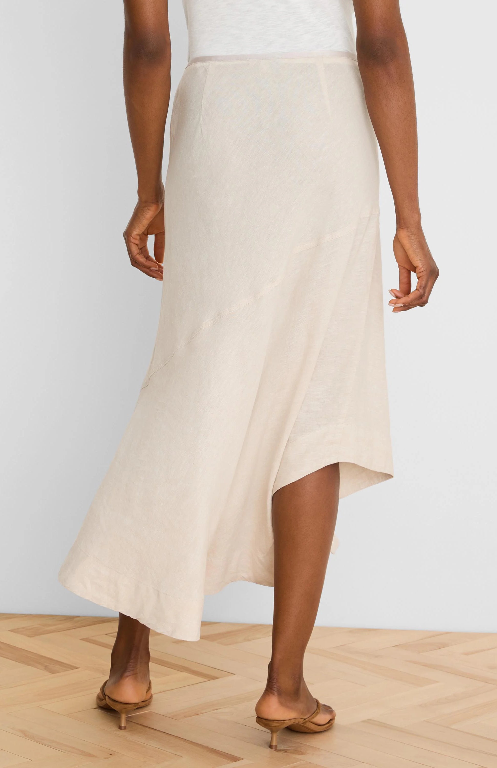 Light beige linen midi skirt, A-line with an asymmetrical hem and visible panel seams, shown from the back.