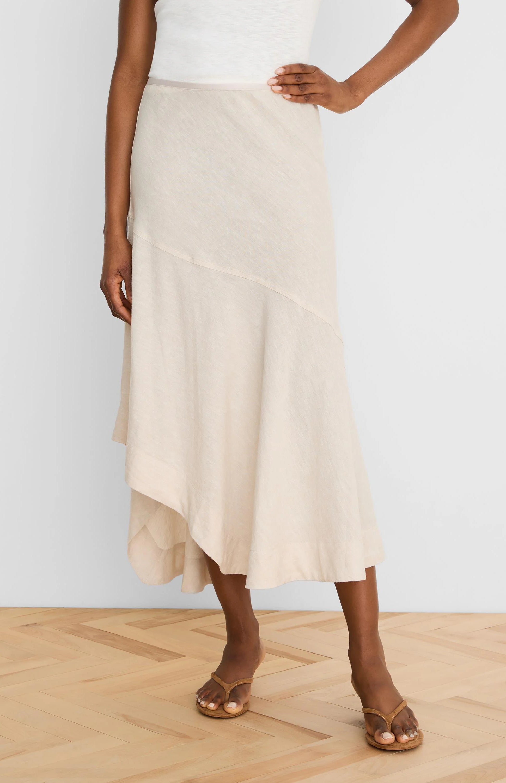 Pale beige linen midi skirt with an asymmetrical, draped hem and diagonal seam.