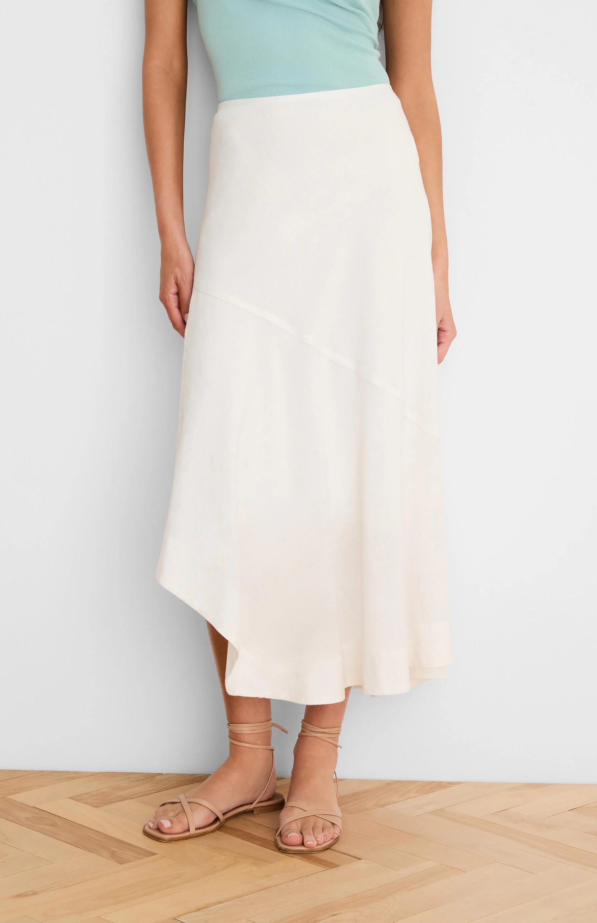 Off-white midi linen skirt with an asymmetric hemline and a diagonal seam detail.