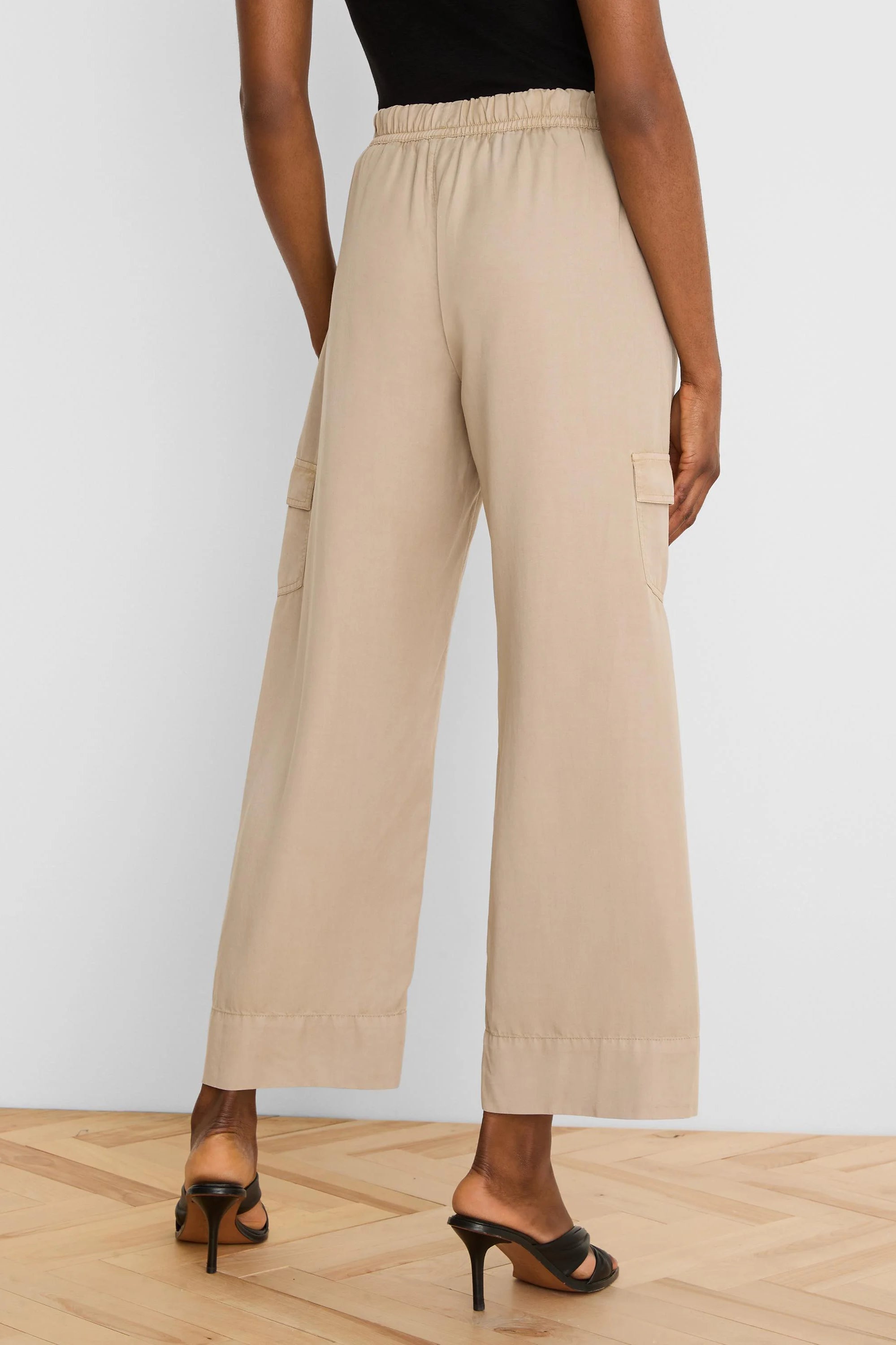 Beige wide-leg drapey cargo ankle pants with elastic waist and side cargo pockets, viewed from behind.