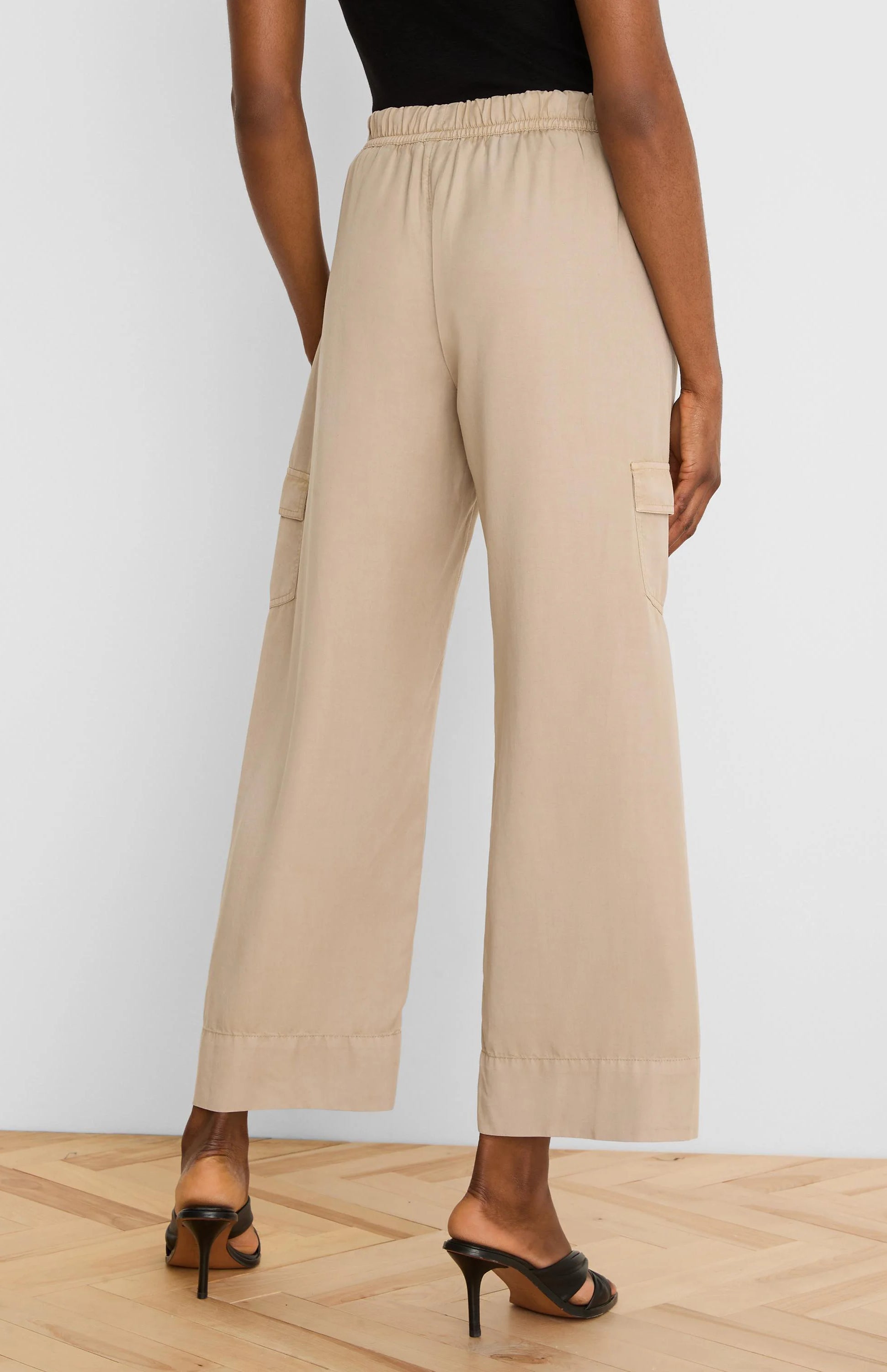 Beige wide-leg drapey cargo ankle pants with elastic waist and side cargo pockets, viewed from behind.