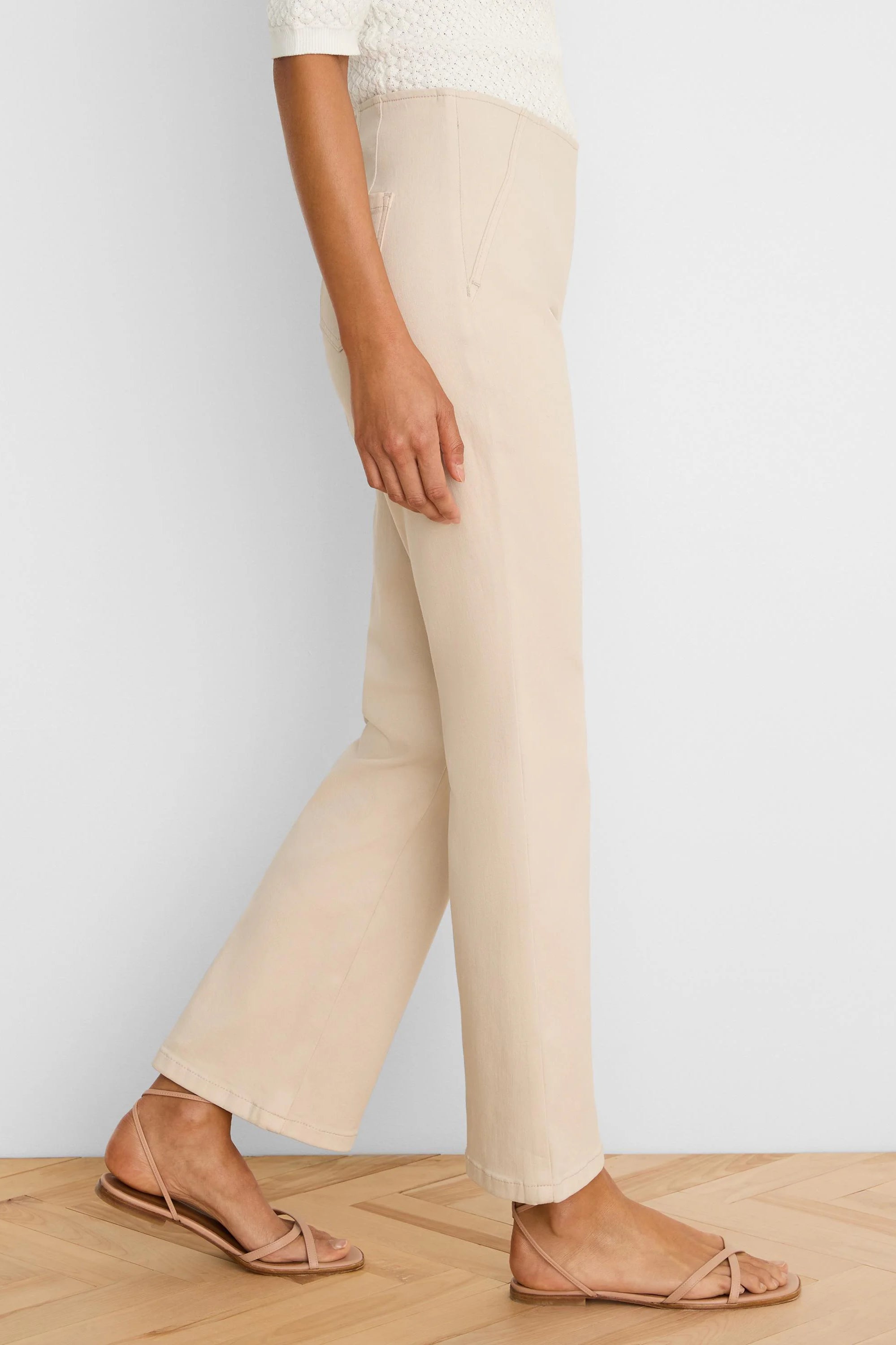 Light beige boot-cut jeans, side view on a model, fitted through thigh, subtle flare at hem.