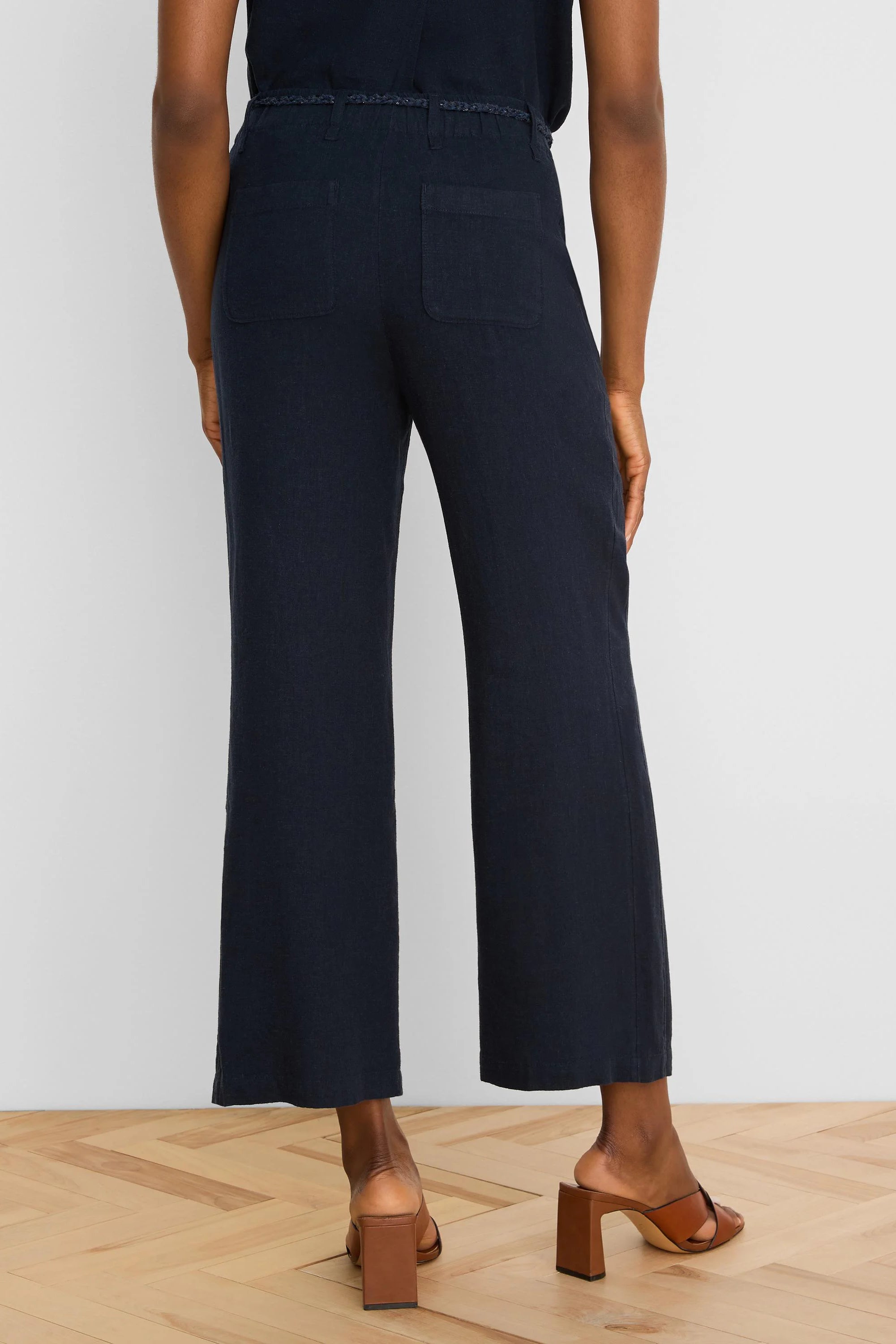 Navy wide-leg linen crop pants with a braided self-belt and two large rear patch pockets, viewed from behind.