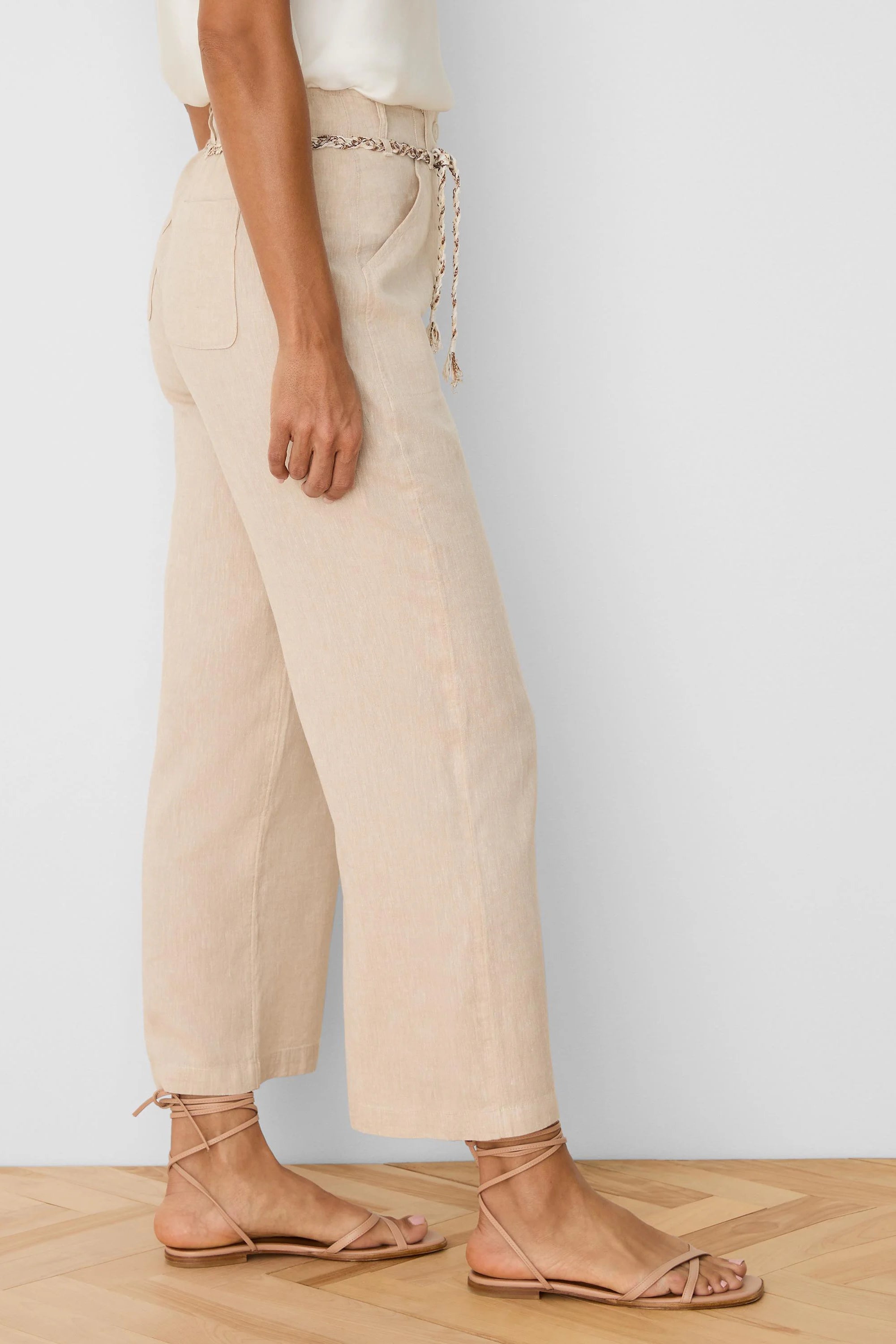 Beige wide-leg linen crop pants with a braided tie belt at the waist and side pockets.