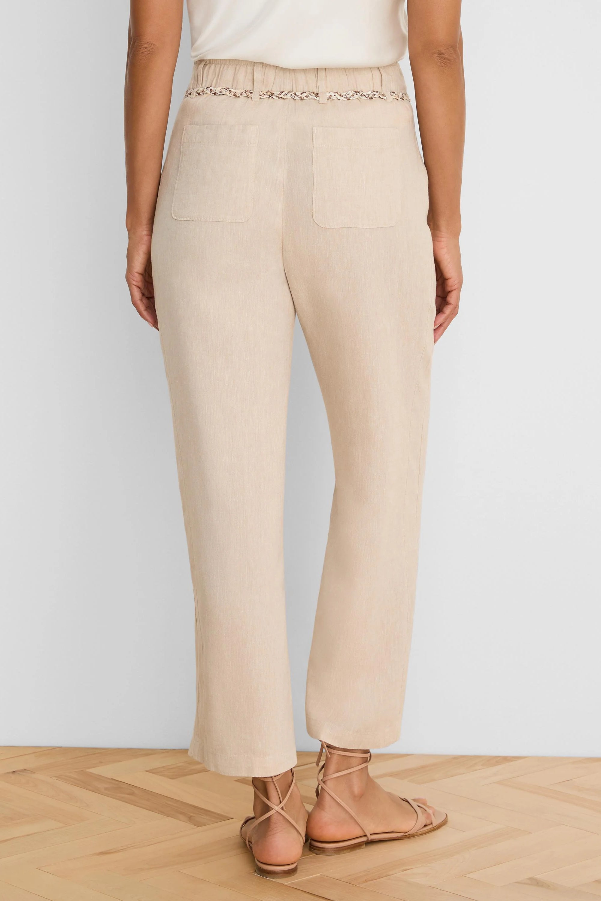 Beige wide-leg linen crop pants, seen from behind. Features a braided belt and two back patch pockets.