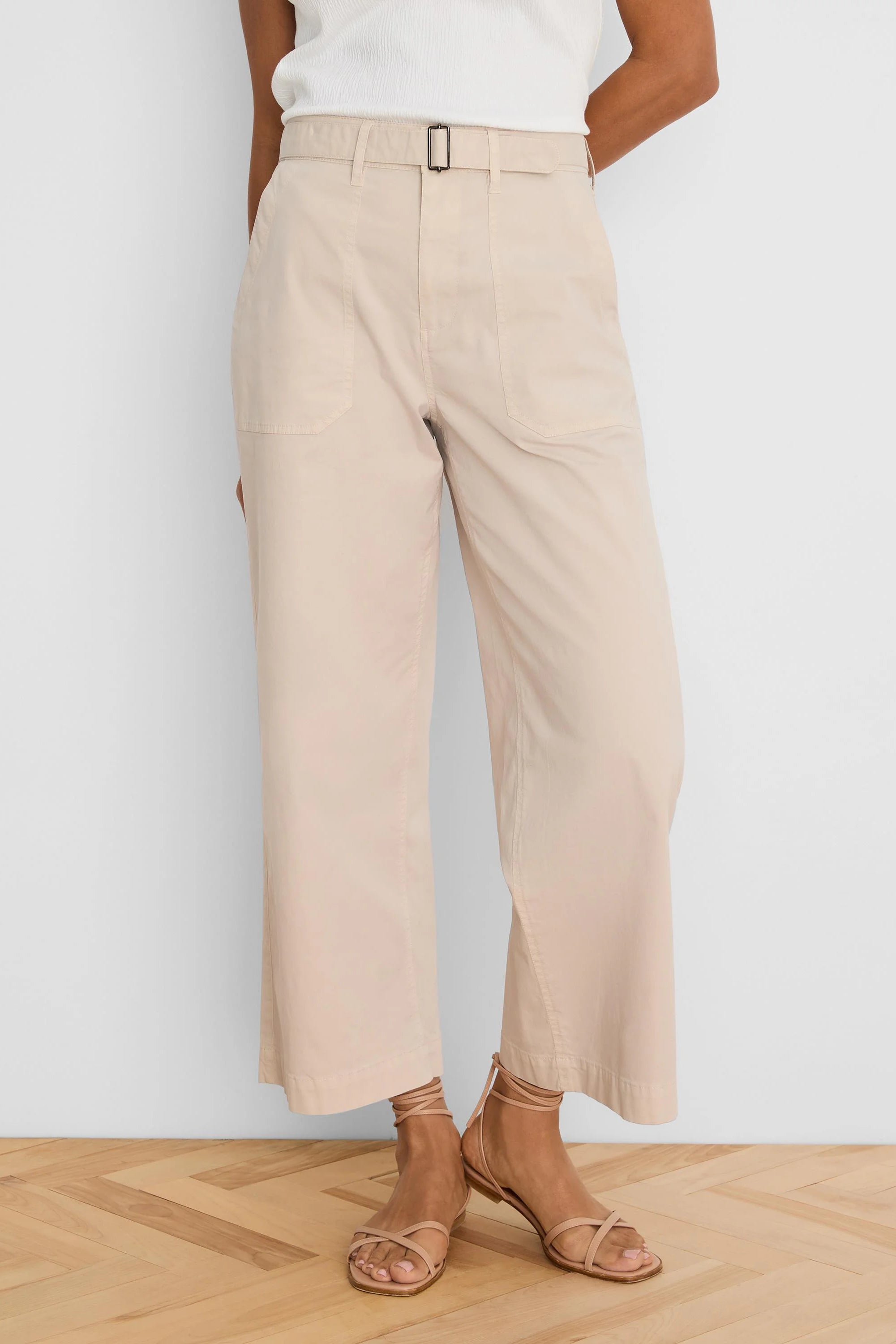 Light beige wide-leg ankle pants with a belted waist, dark rectangular buckle, and large front patch pockets.