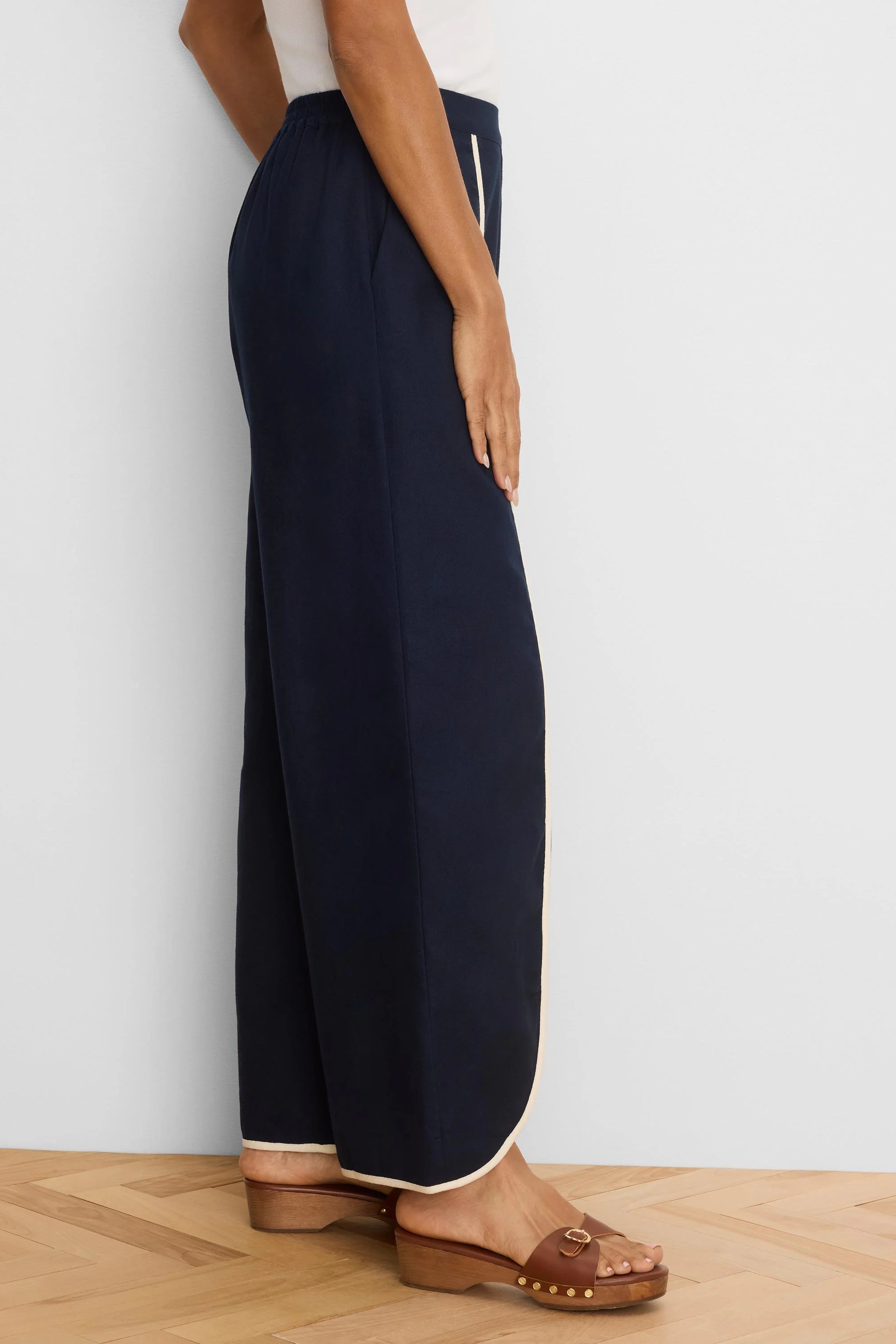 Dark navy wide leg pants, shown from side, with cream piping down side seams and around hems.