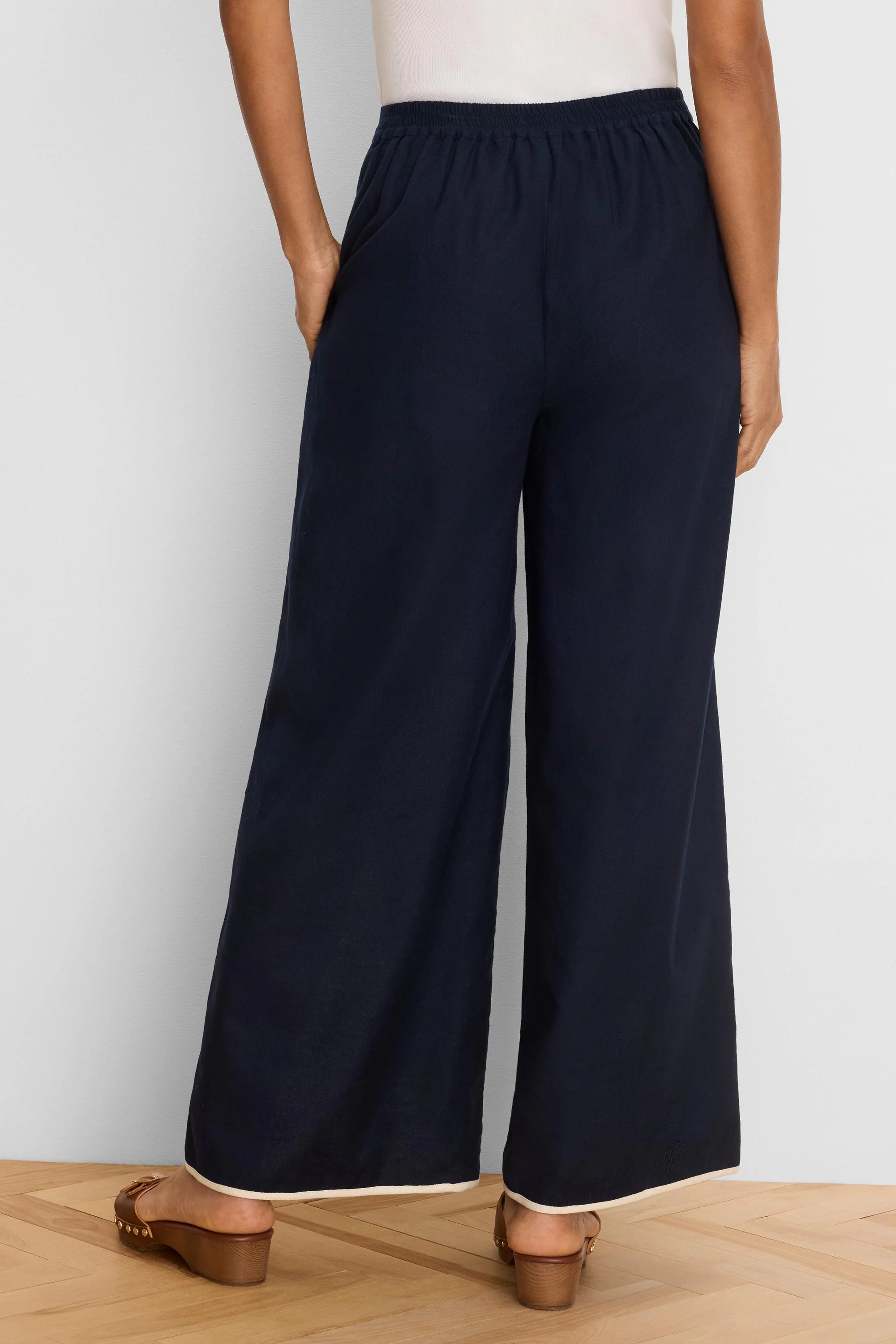Rear view of navy wide leg pants with an elasticized waist and light-colored piping along the hem.