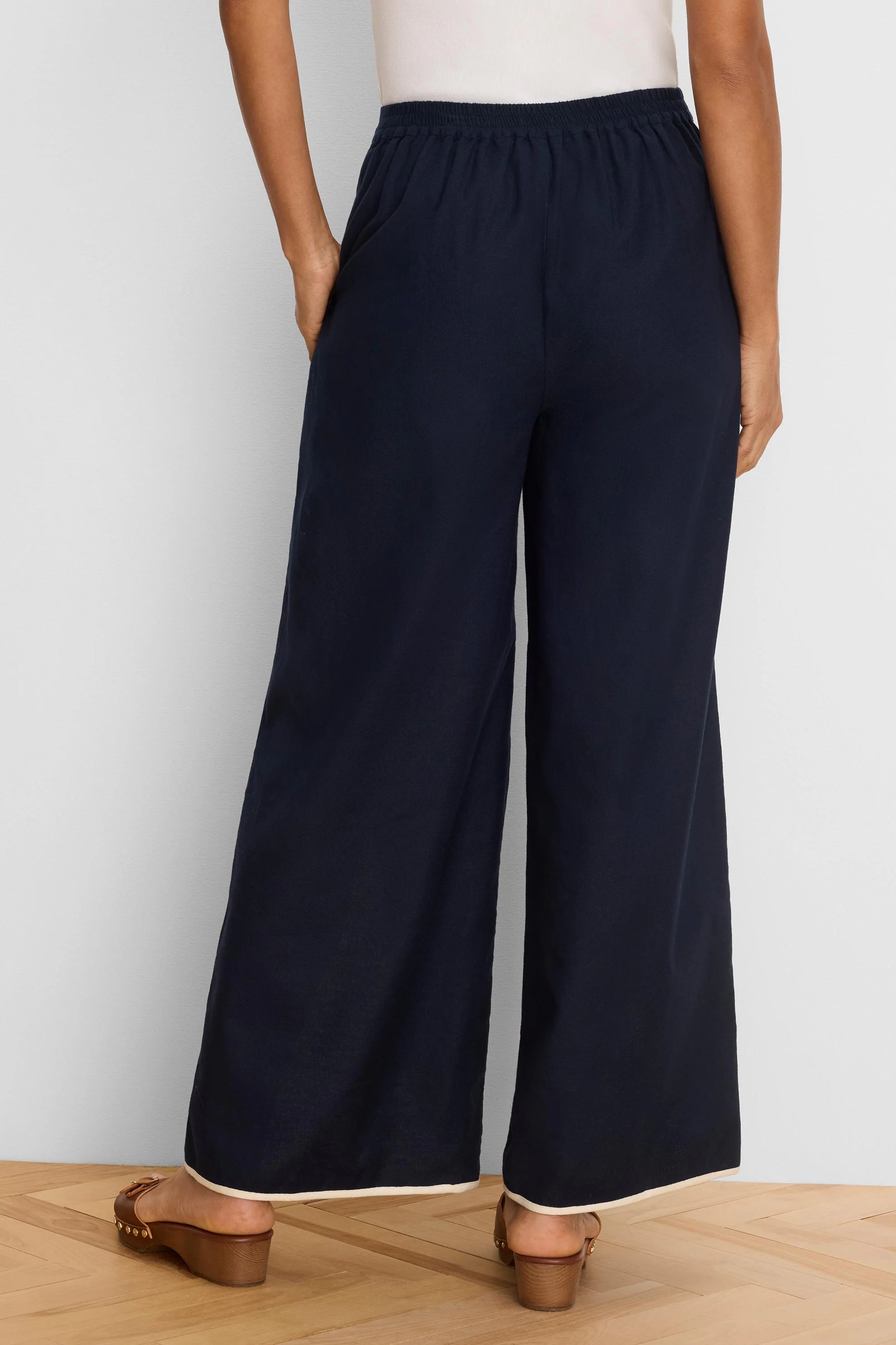 Rear view of navy wide leg pants with an elasticized waist and light-colored piping along the hem.