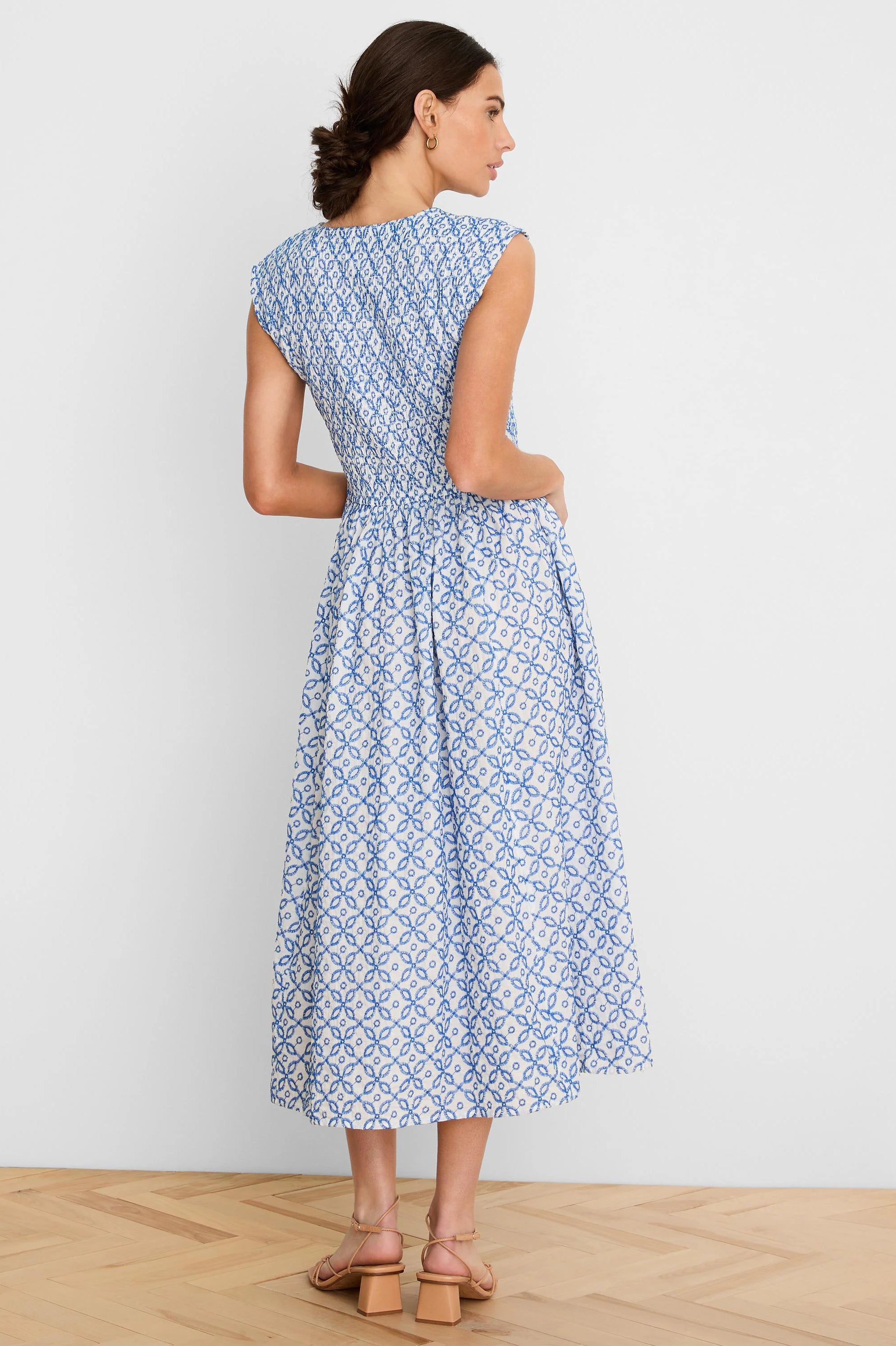 White sleeveless midi dress with blue embroidered tile pattern and smocked bodice.