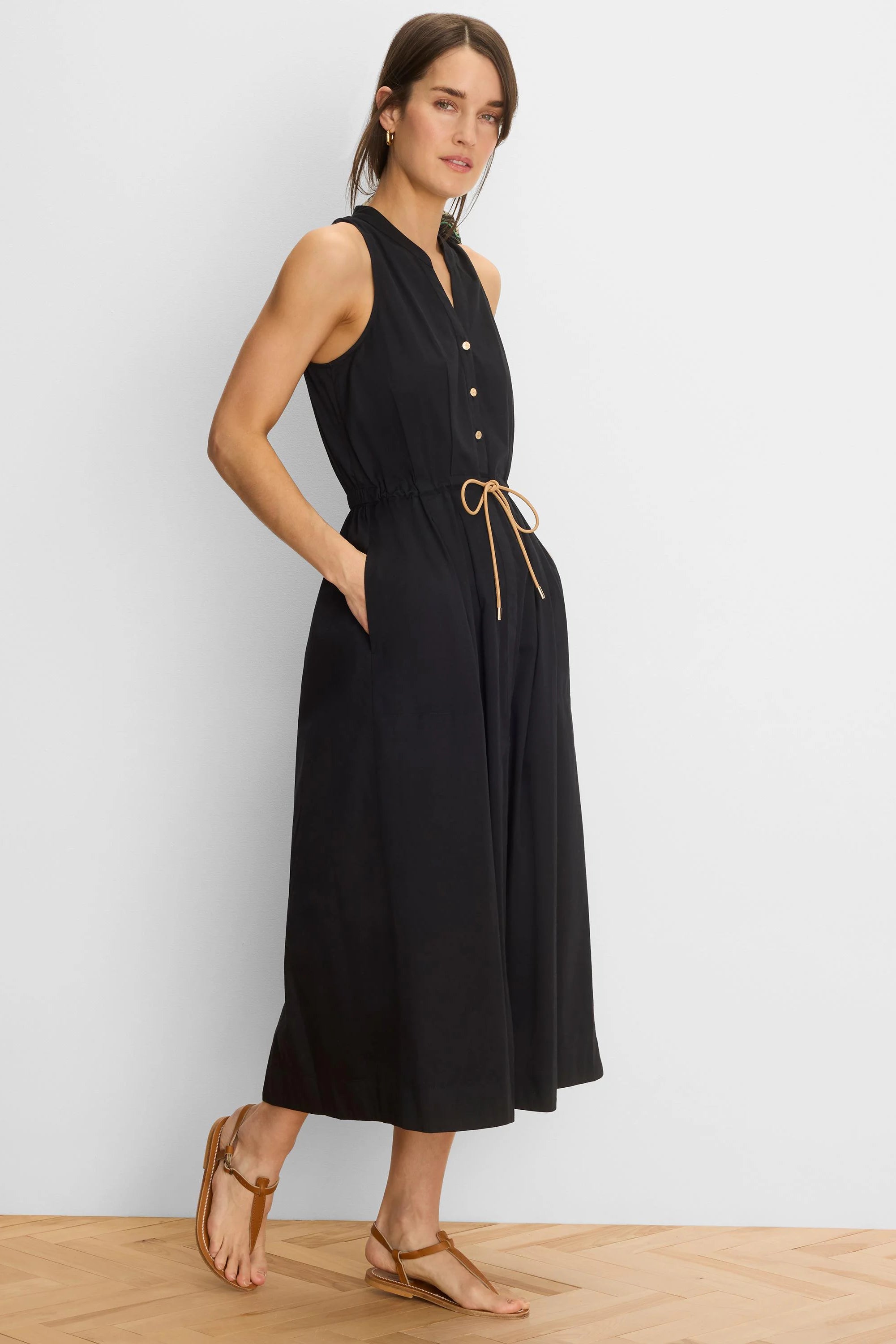 Black sleeveless V-neck midi dress with gold buttons, drawstring waist with tan tie, and side pockets.