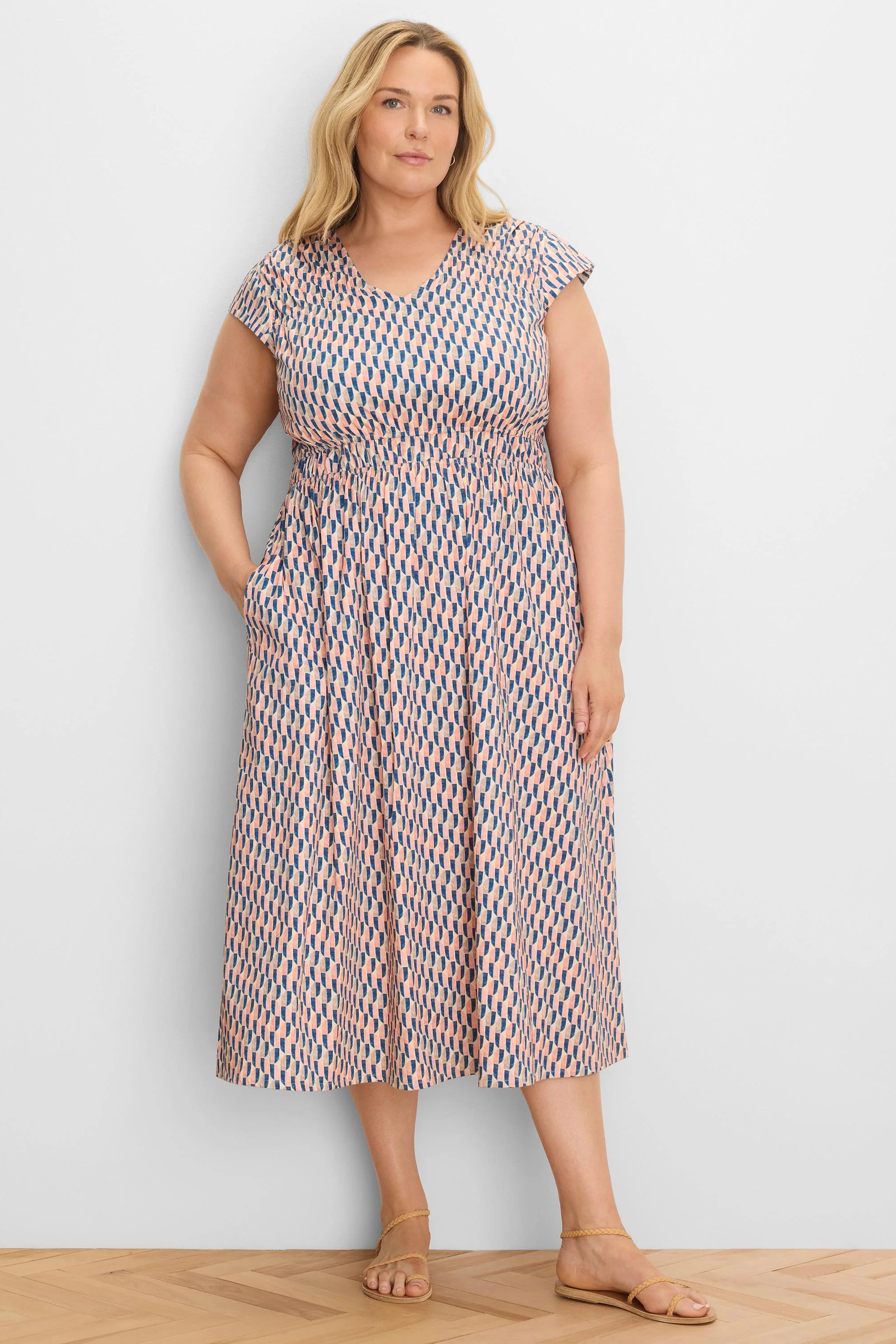 Model in peach and navy geometric print V-neck cap sleeve midi dress with smocked waist and pockets.