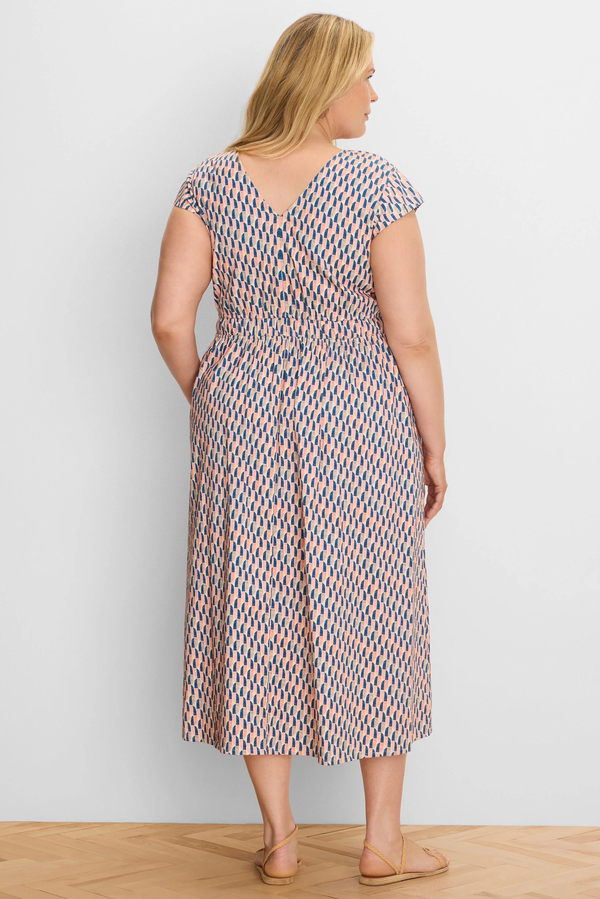 Midi dress with cap sleeves, V-back, and elasticated waist. Features a peach, navy, and tan geometric pattern.