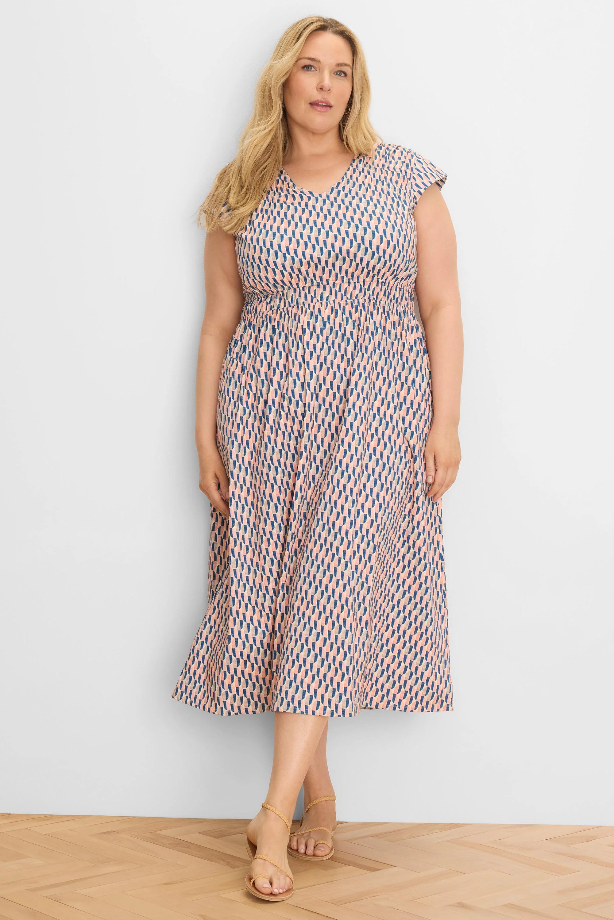 Peach V-neck midi dress with cap sleeves, shirred waist, and blue/gray geometric pattern.