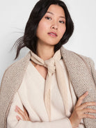 Light beige knitted scarf, tied in a knot around the neck. Visible ribbed texture.