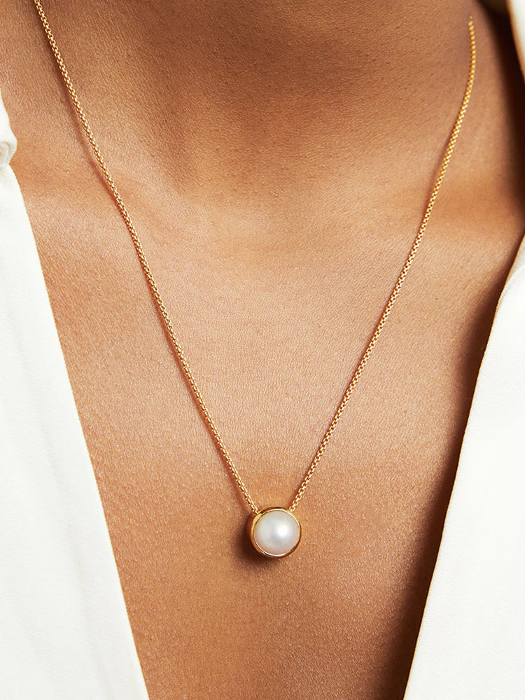 Gold chain necklace with a single, round, off-white pearl pendant.