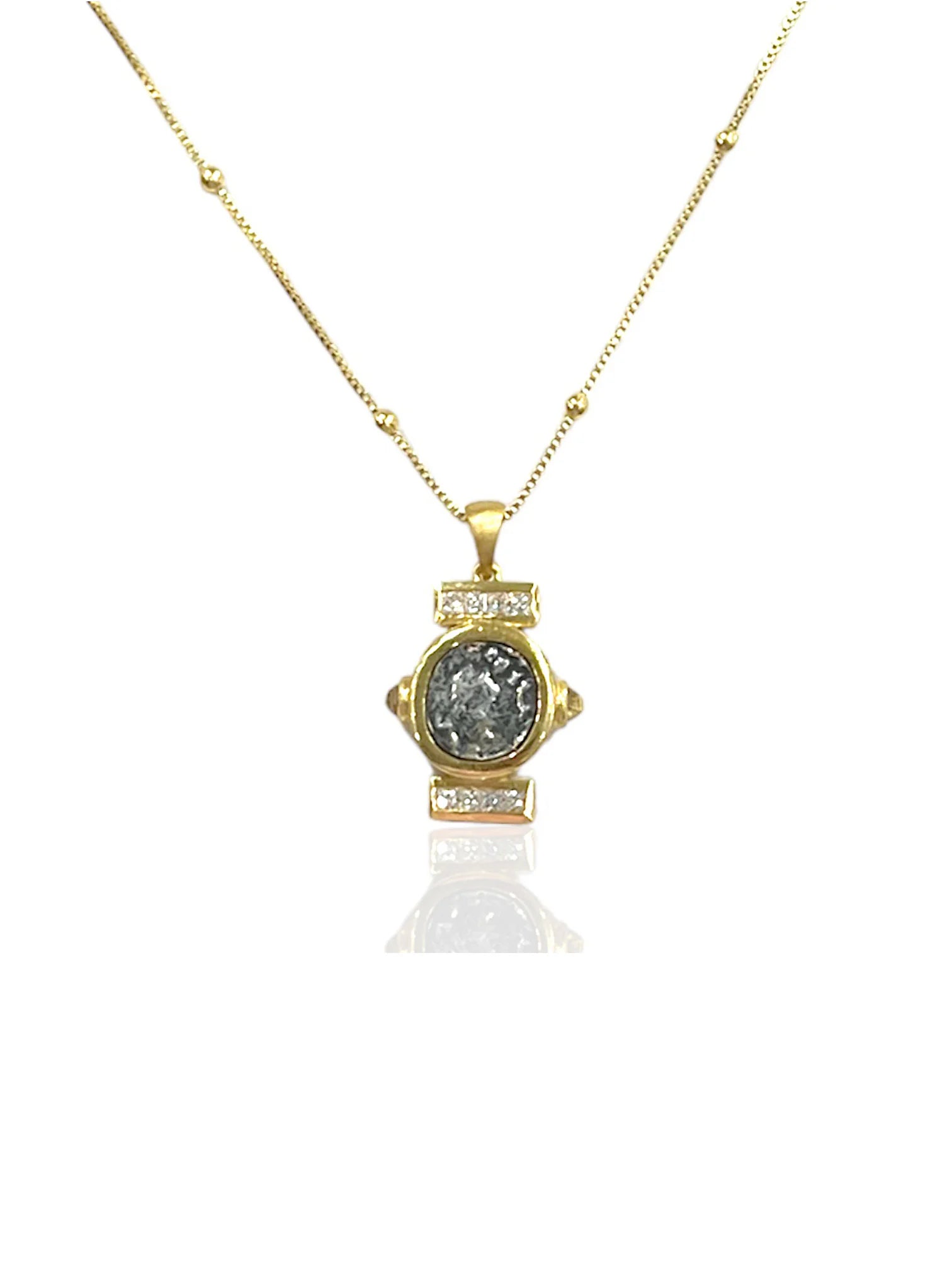 Gold beaded chain necklace. Pendant features a central textured dark gray coin, framed by gold and clear stones.