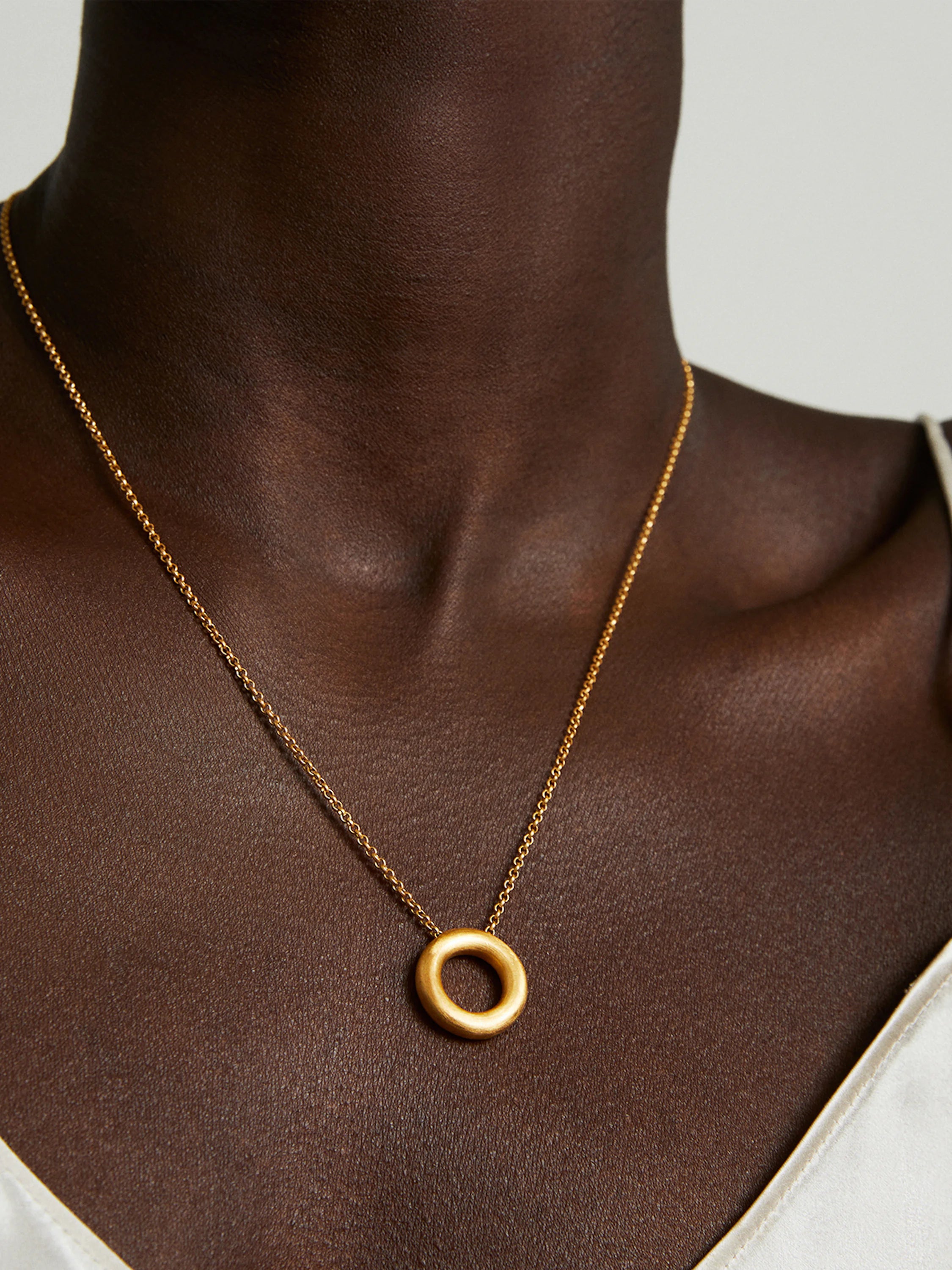 Gold chain and circular pendant necklace on dark brown skin.