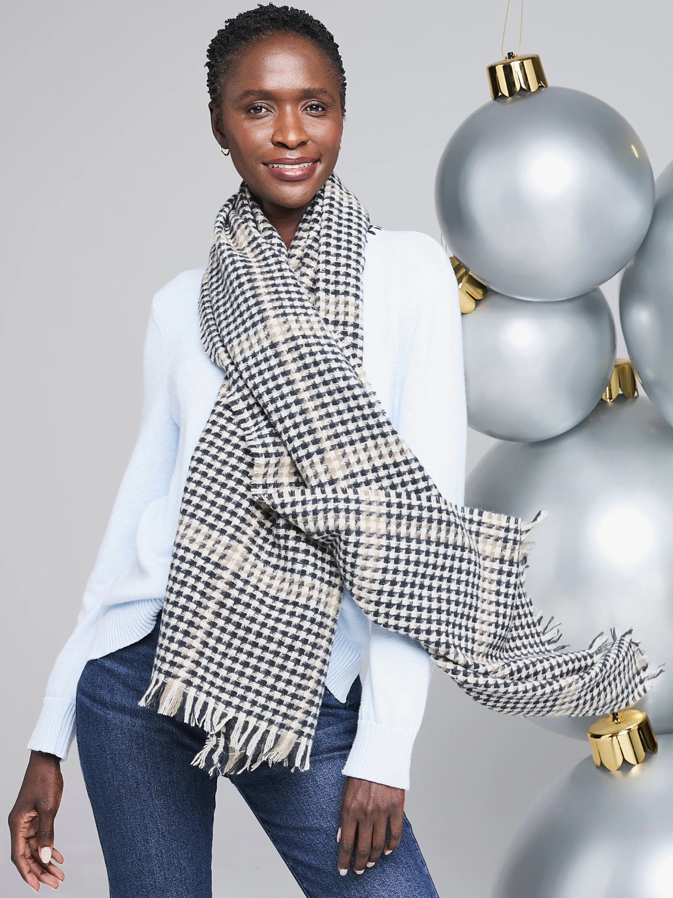 Scarf with dark grey, cream, and tan small check pattern. Features fringed ends and is draped around the neck.
