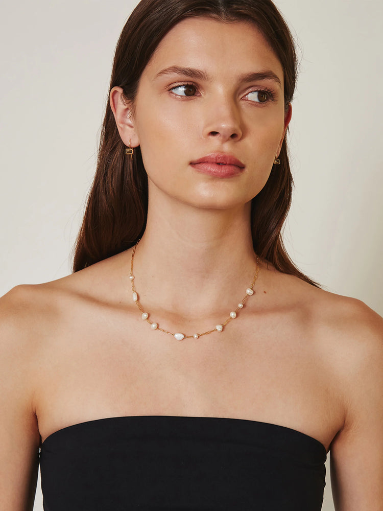 Gold chain necklace with varying sized off-white pearls.