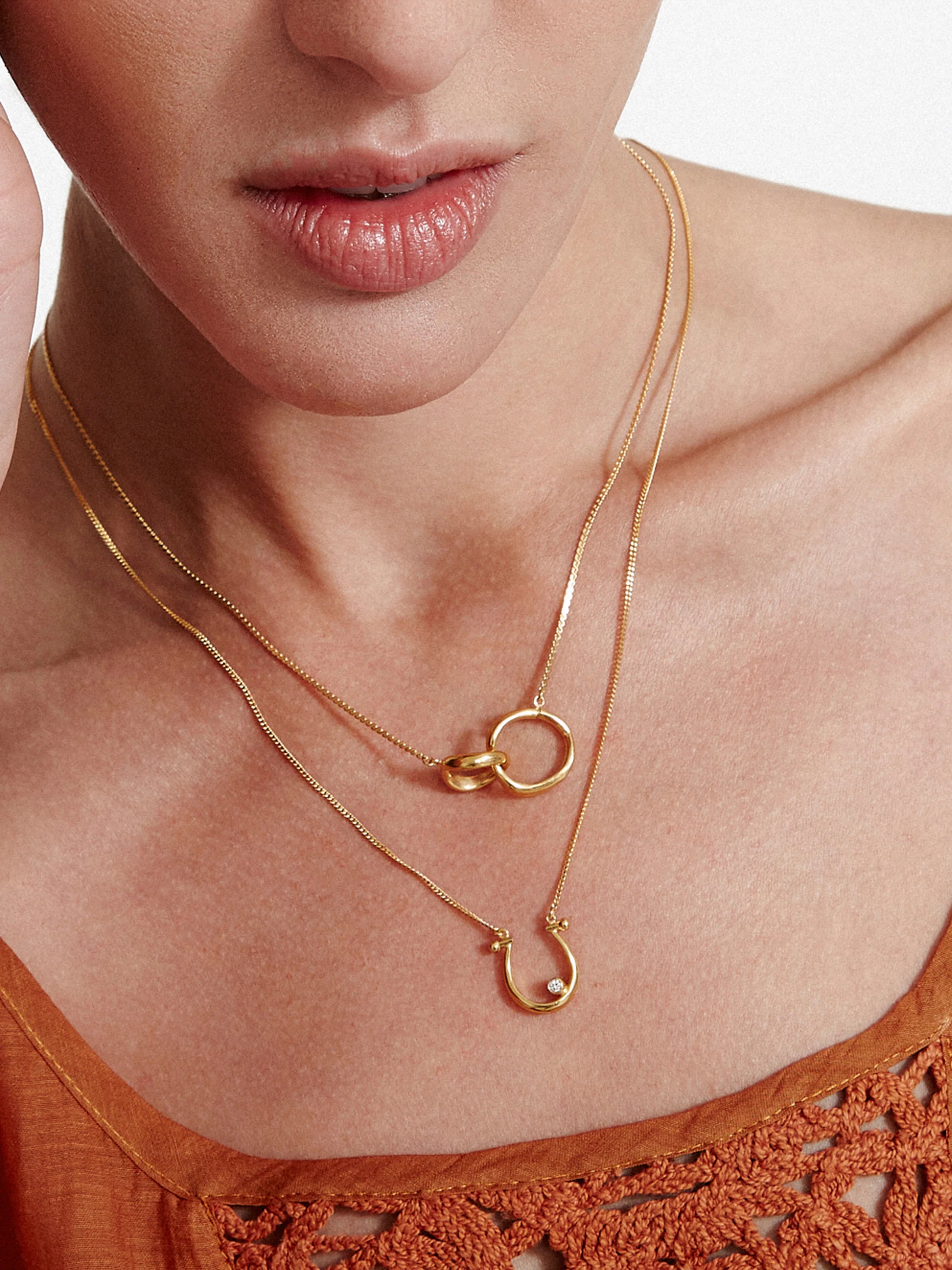 Gold double-loop necklace. Layered beneath it is a gold chain with a small diamond horseshoe pendant.