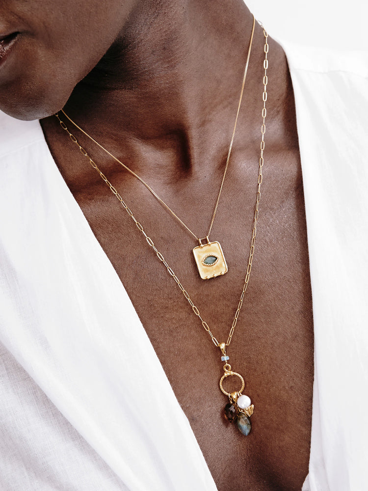 Two layered gold necklaces. Top: rectangular gold pendant with green stone. Bottom: paperclip chain with mixed...