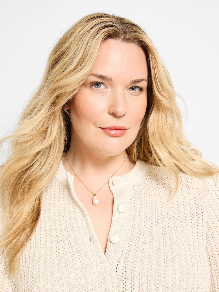 Gold chain necklace with a single, light pink, irregular drop pearl, shown worn by a model.