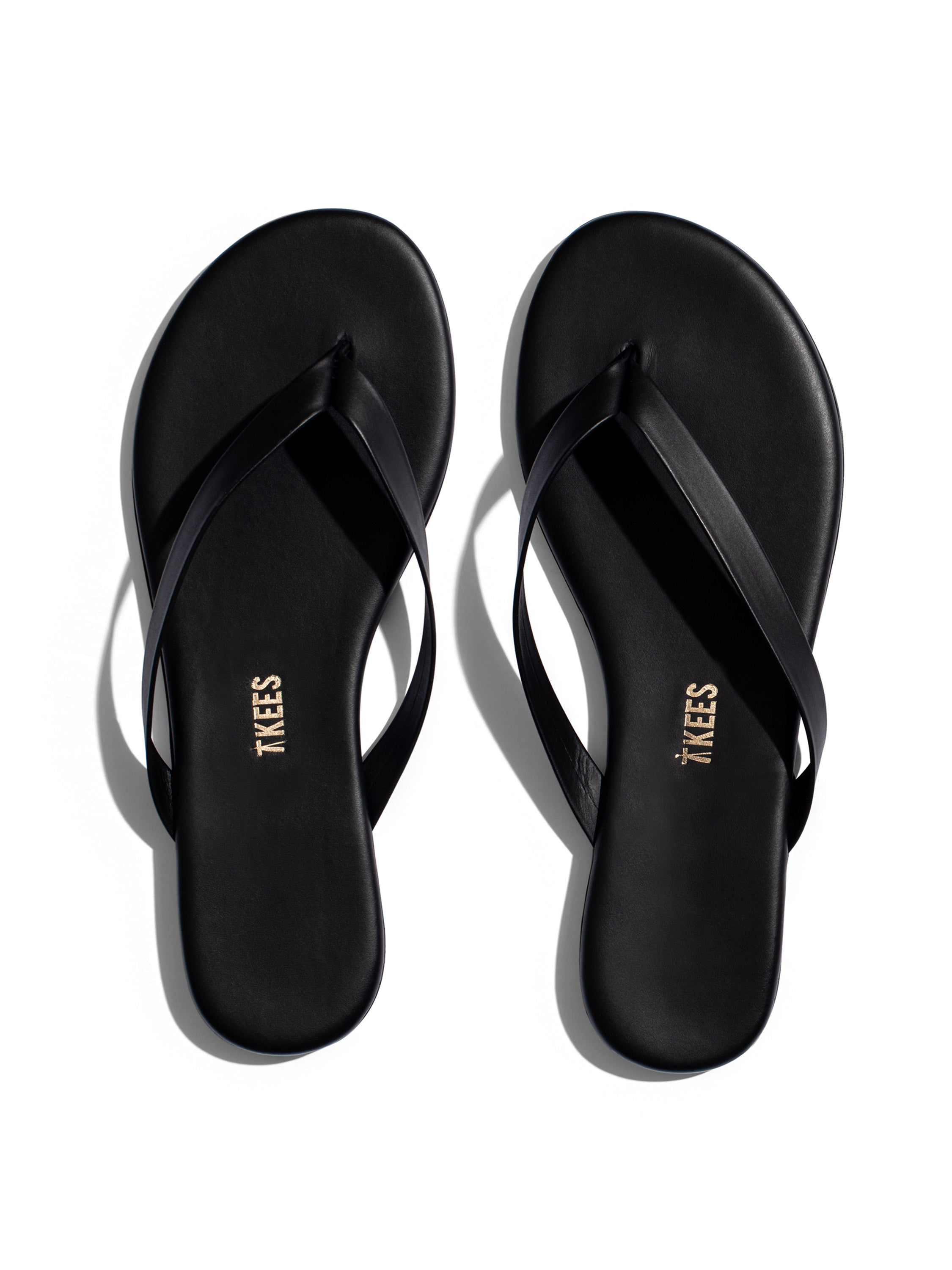 Black minimalist leather flip-flops featuring thin straps, a thin sole, and subtle gold branding on the footbed.