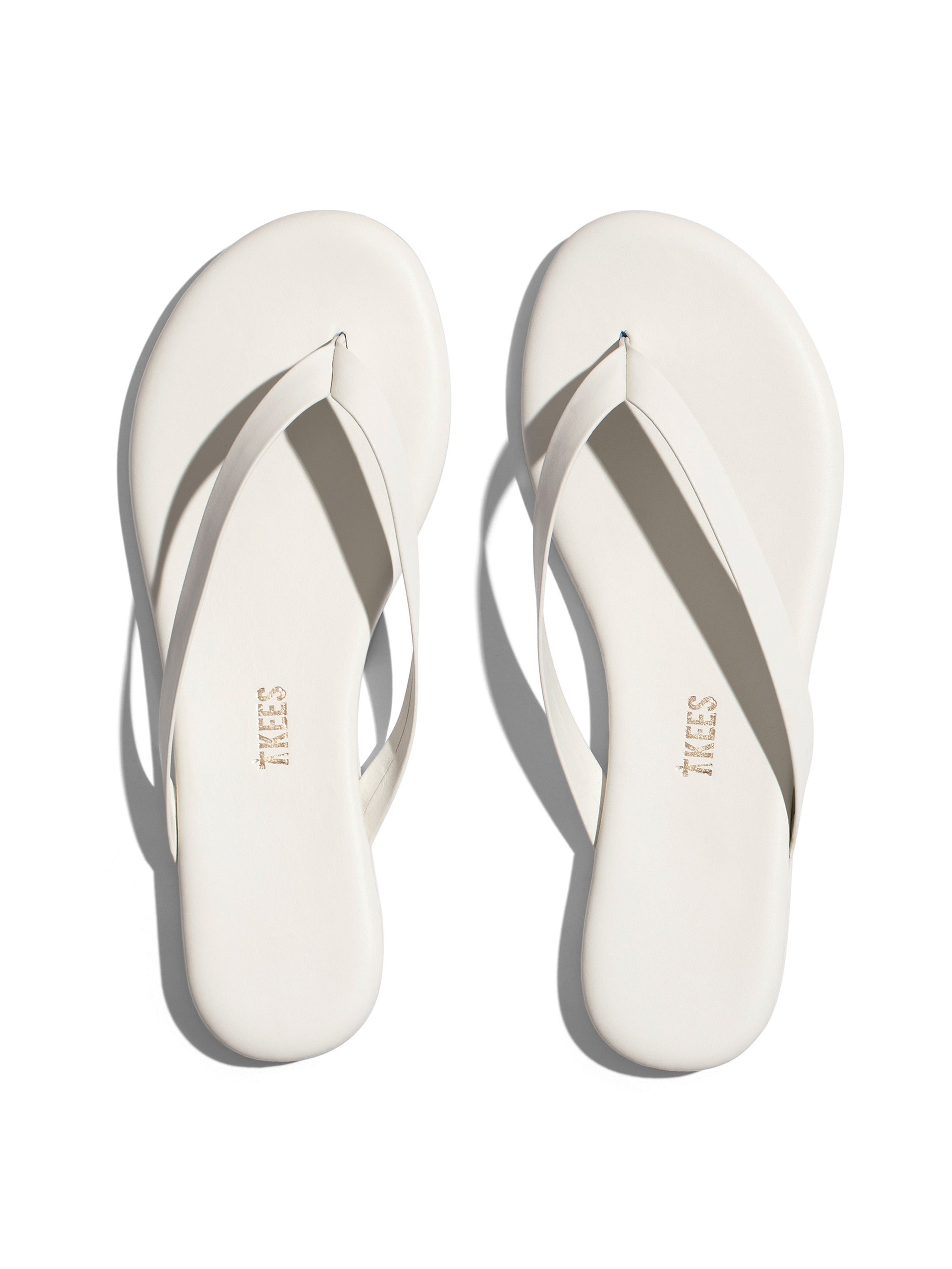 A pair of off-white leather flip-flops with thin straps and a flat sole exhibits a simple, minimalist design.