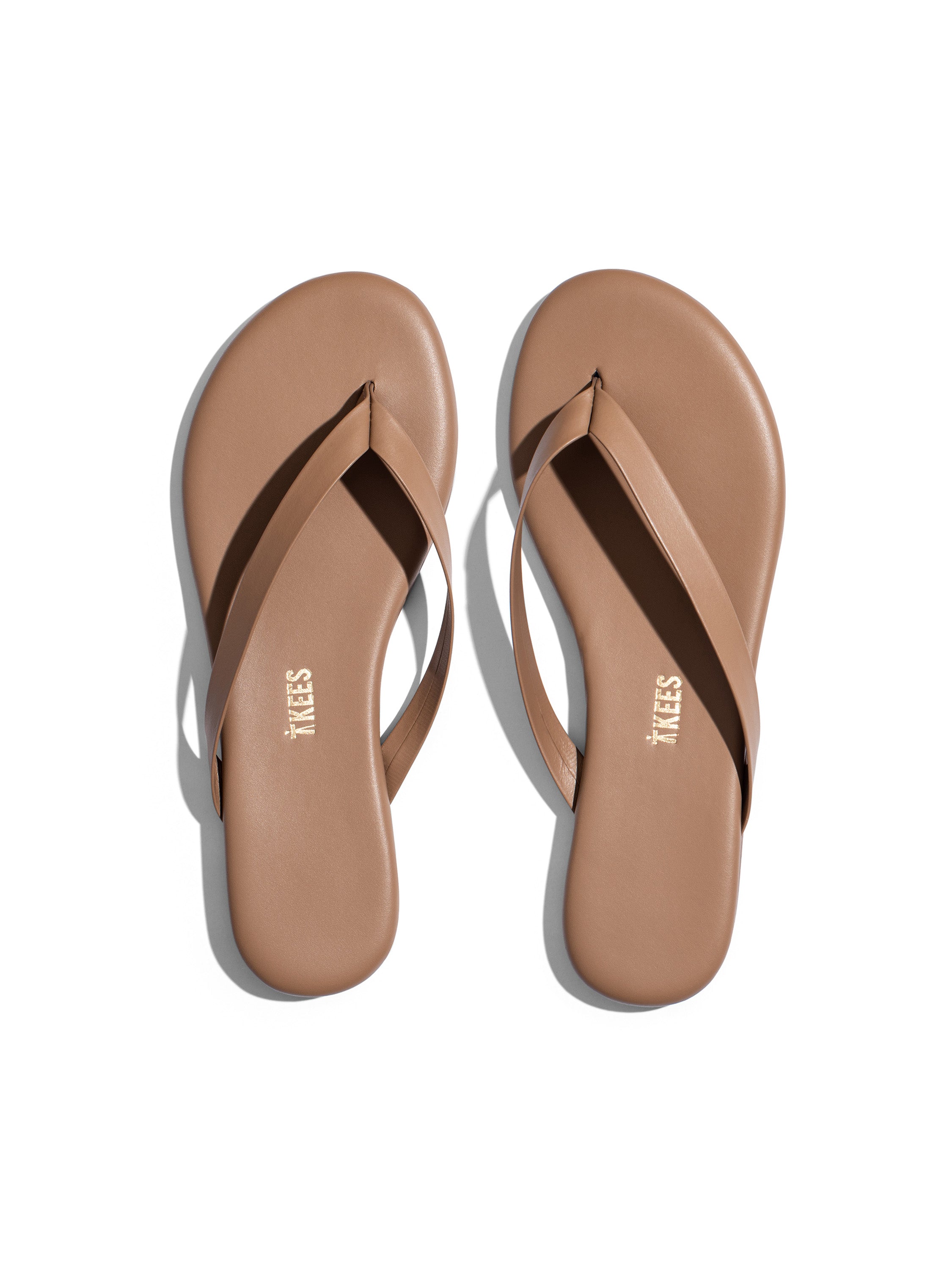 The flat, minimalist nude leather flip-flops feature thin straps and a simple, rounded sole design.