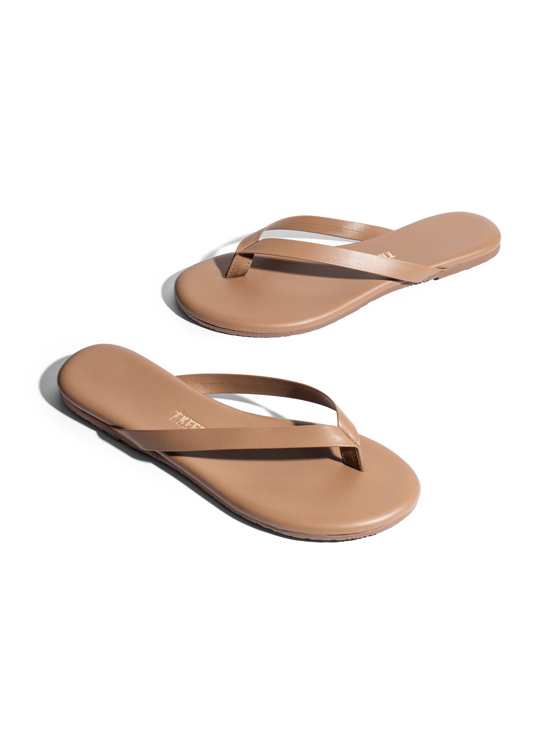 Tan flat leather flip-flops feature thin, minimalist thong straps and a simple rubber sole.